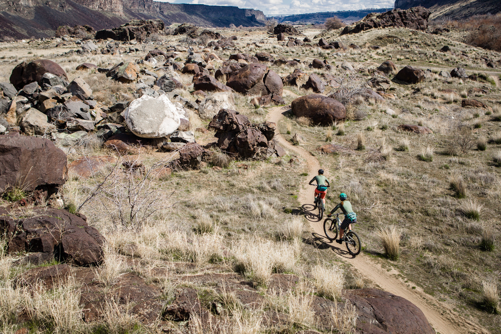 Two cyclists riding on a dirt path through rocky terrain in a natural landscape.