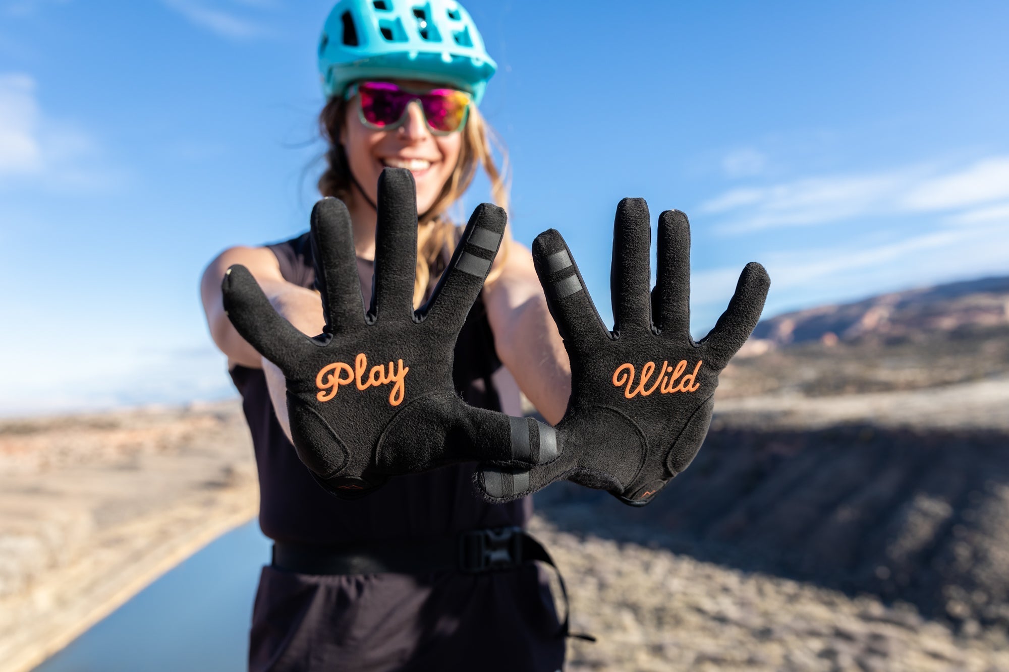 A person wearing gloves with the words 'Play' and 'Wild' displayed, smiling outdoors.