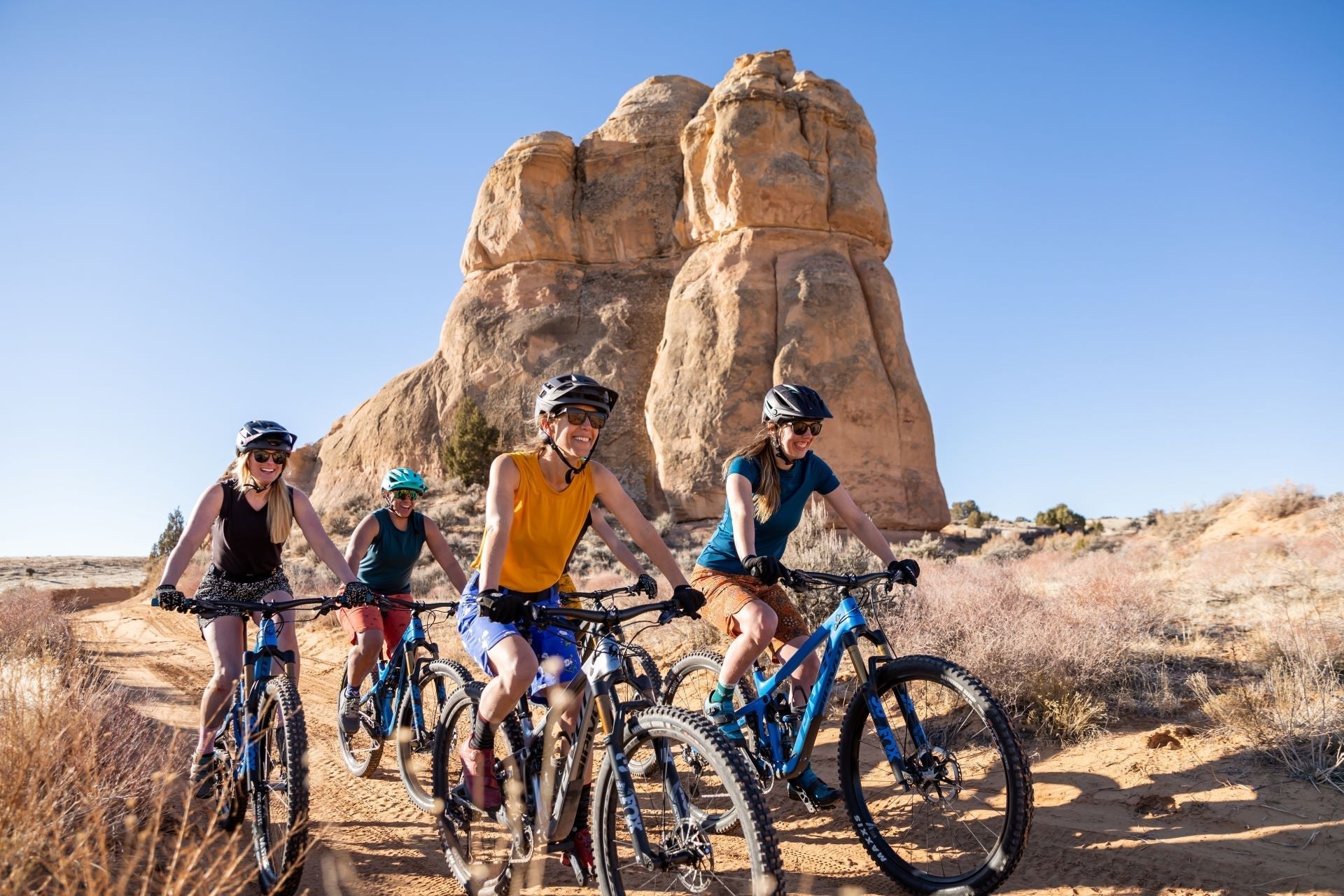 Four women biking in a desert landscape with rock formations in the background