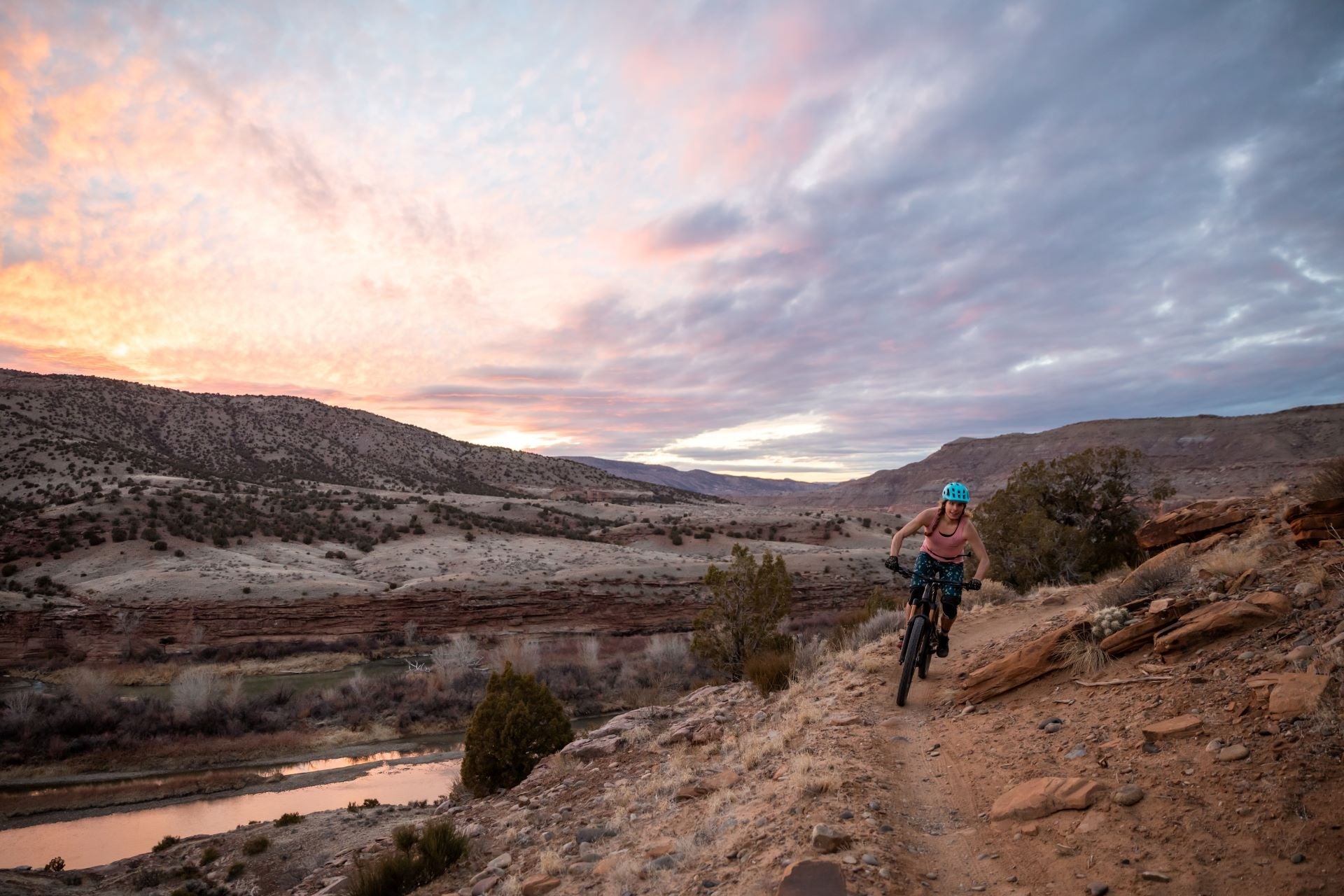 A woman biking on a trail during sunset with mountains in the background