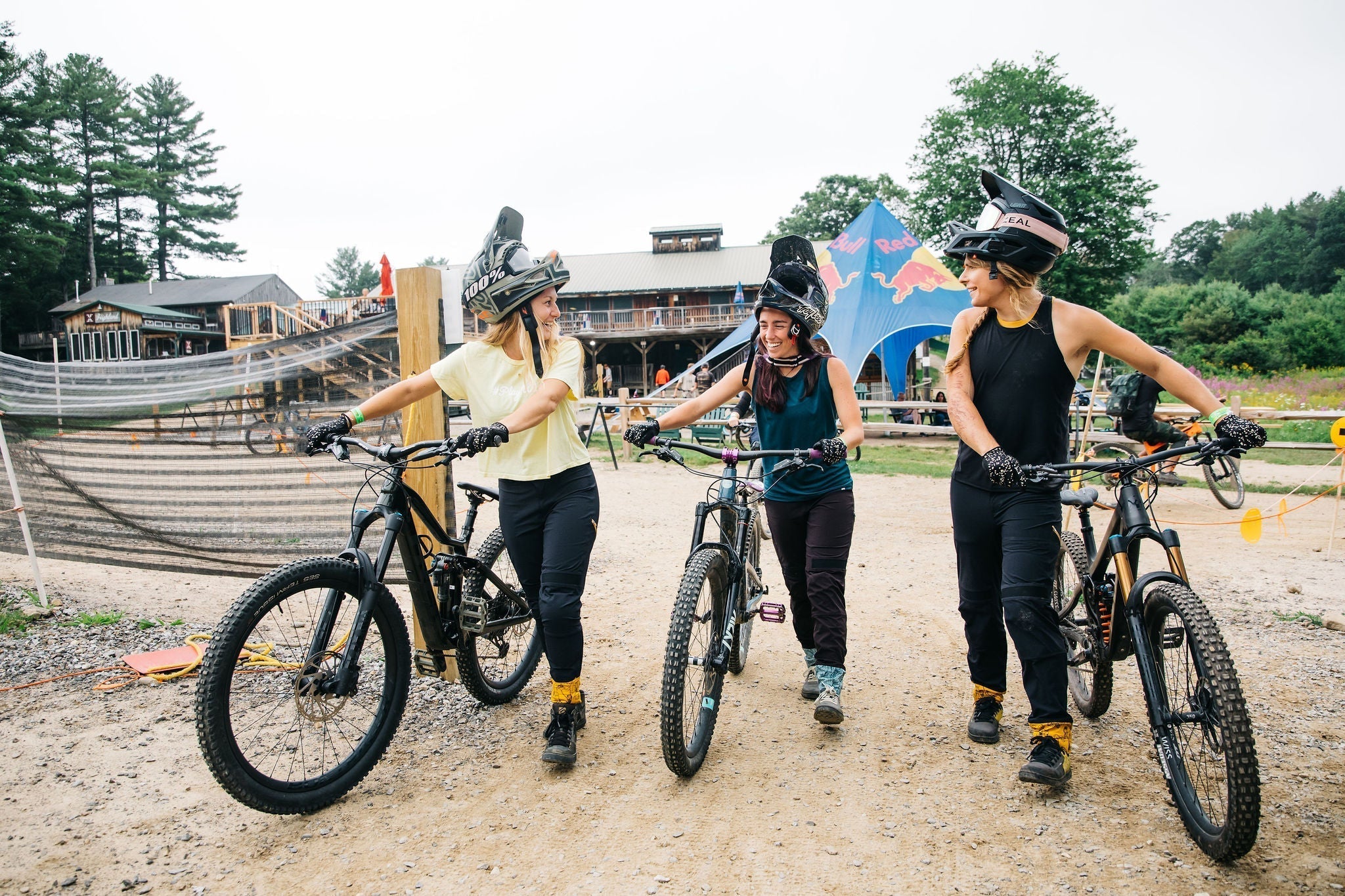 Three female bike mechanics chatting while riding mountain bikes in a scenic outdoor setting.
