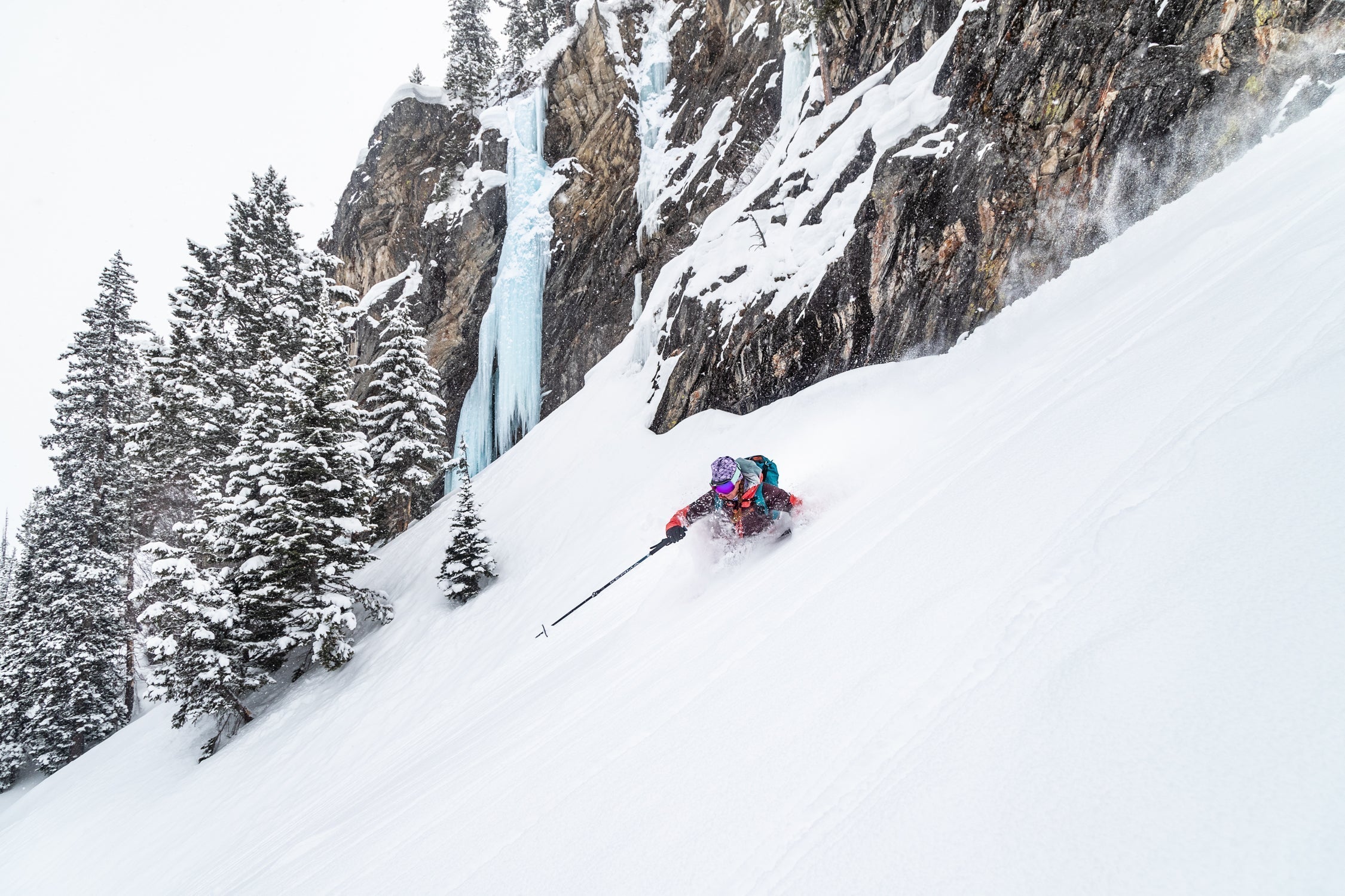 A female skier navigating through deep snow with a waterfall in the background.