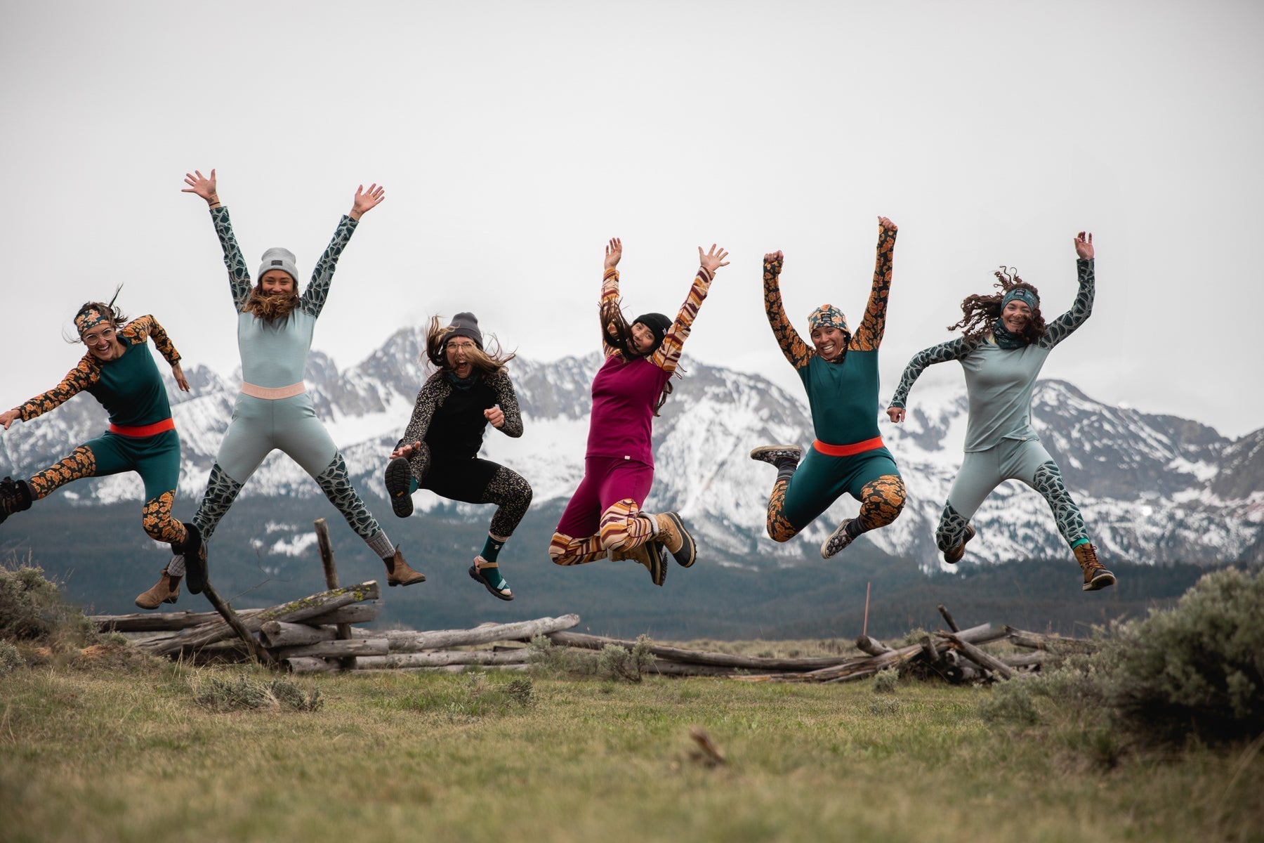 A group of women in colorful outfits jumping joyfully in a mountainous landscape.