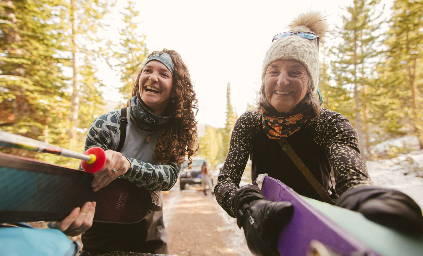 Two women smiling and holding snowboards in a forest setting