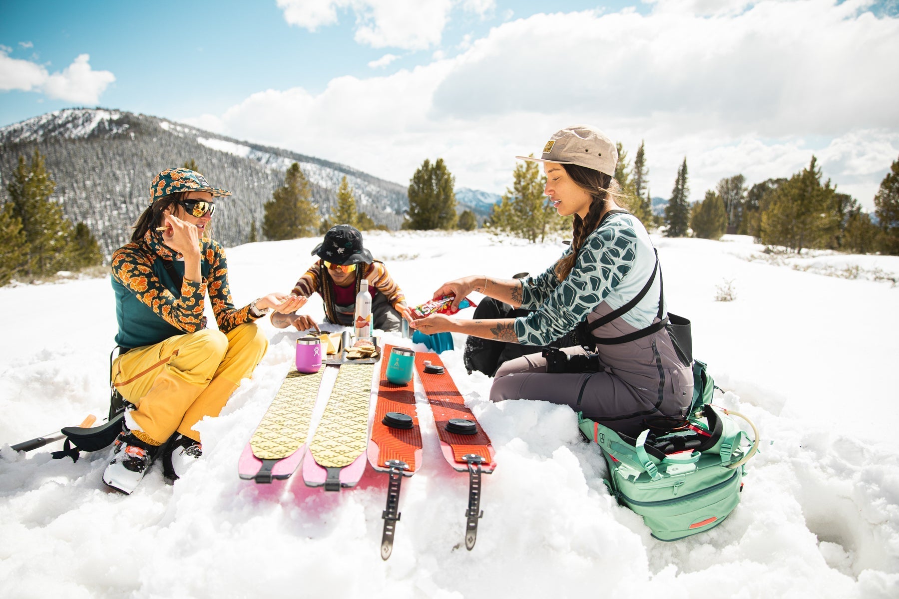 Three women enjoying a picnic in the snow with skis nearby, promoting women-led brands.