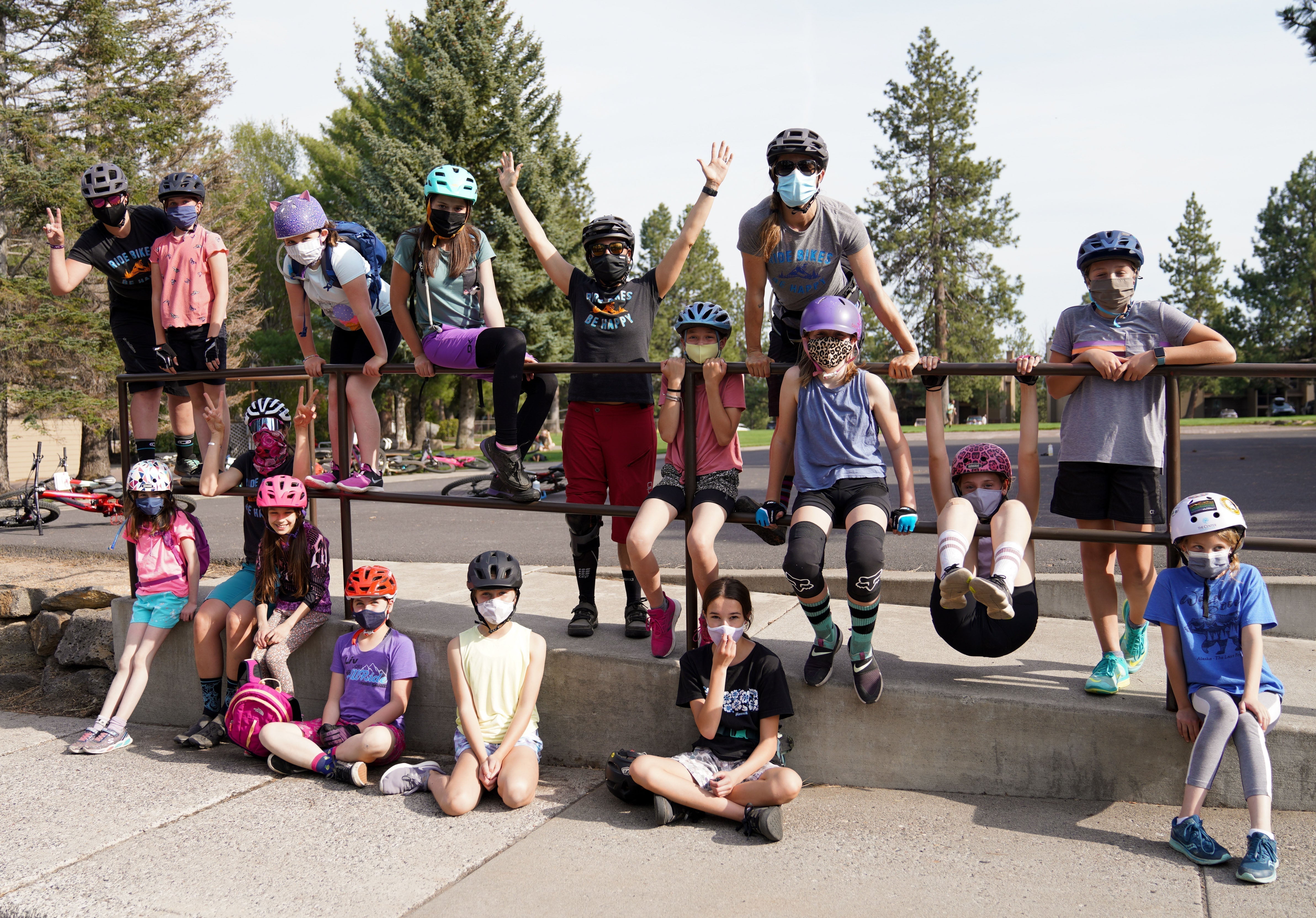 Group of young girls in helmets and masks, posing with bikes in a park setting.