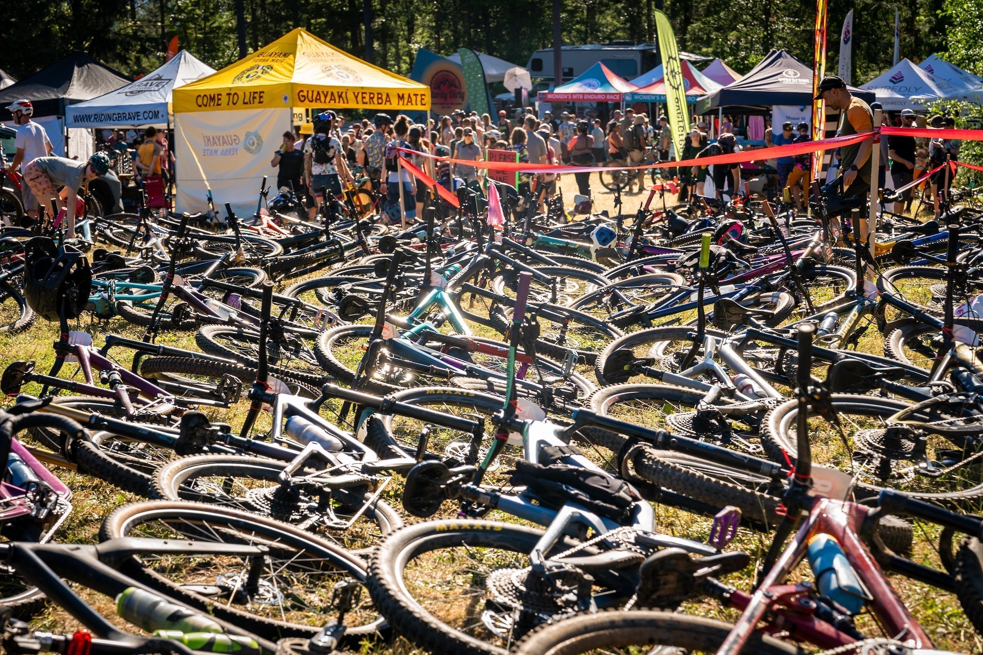 A crowded bike area at the Sturdy Dirty 2024 event, with many bikes on the ground and tents in the background.