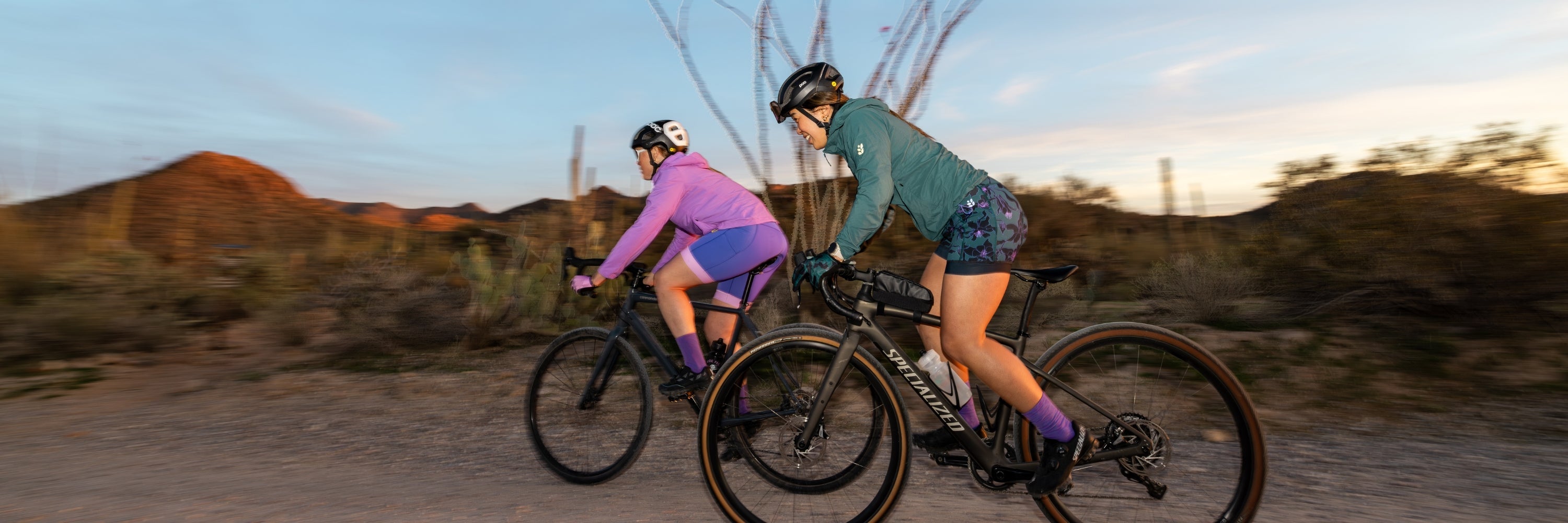 Cyclist wearing a pink top and floral shorts riding a black bicycle on a forest trail, motion blur in background
