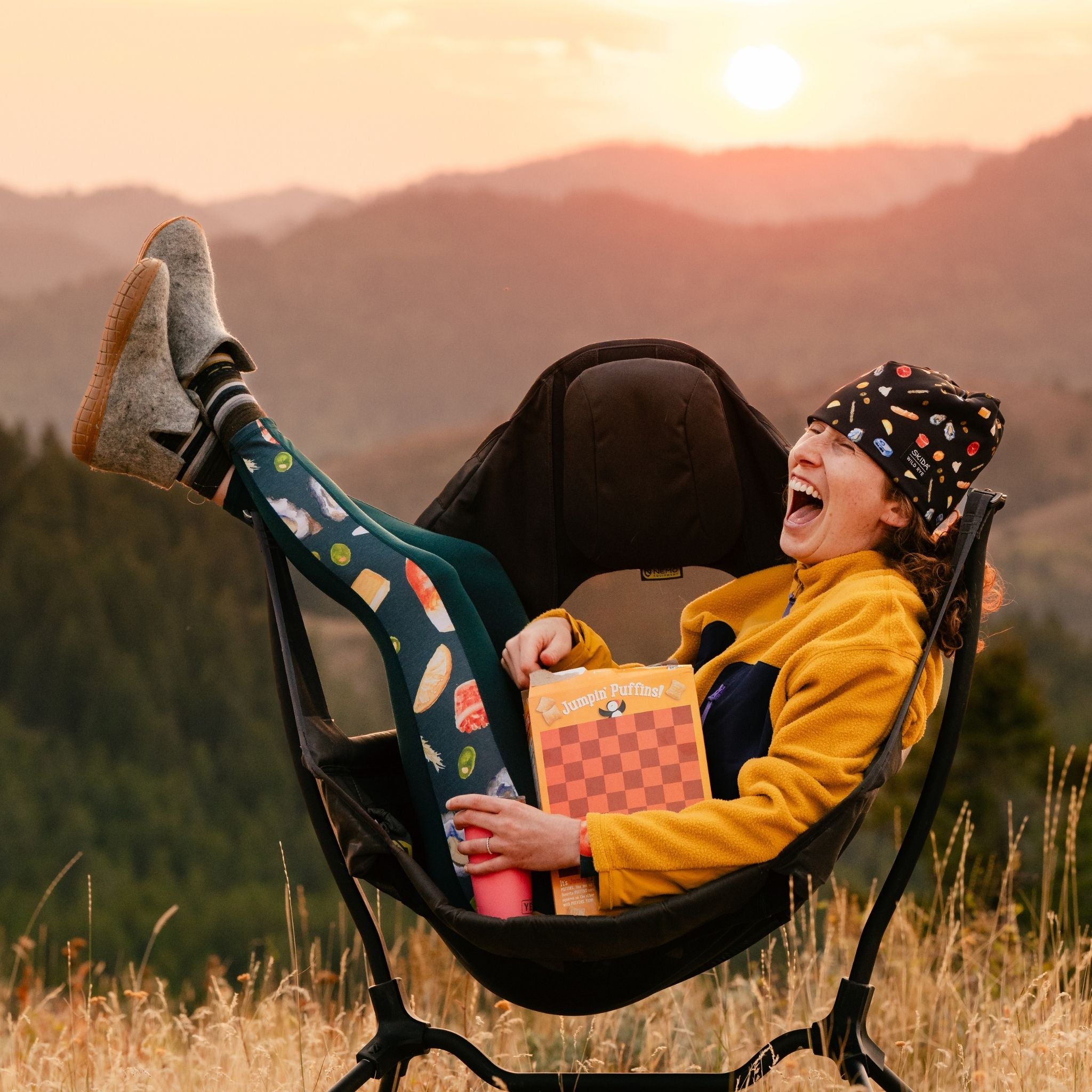 Person sitting in a camping chair with a book, enjoying a sunset in the mountains.