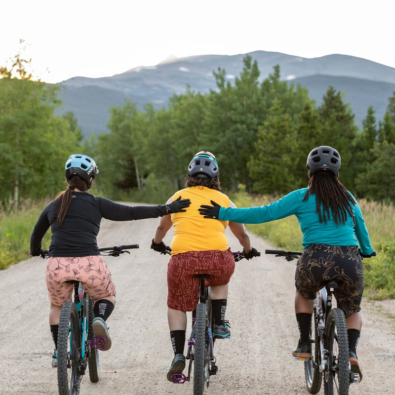 3 women riding bikes down gravel road