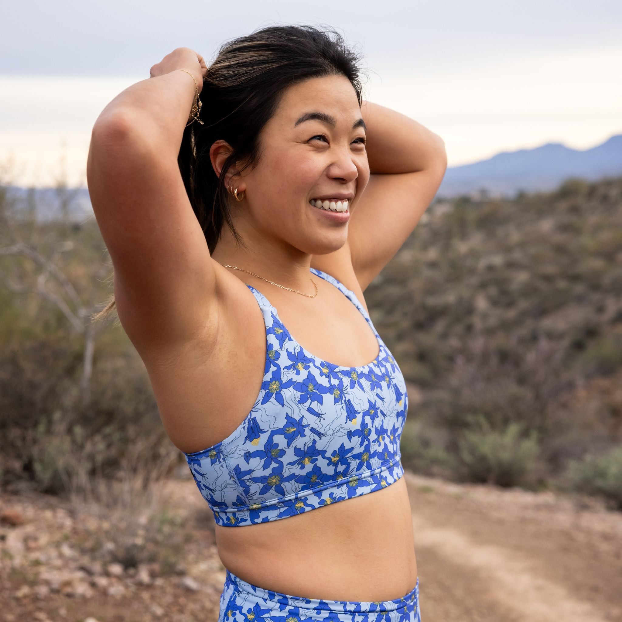 Woman wearing a blue floral sports bra and shorts outdoors, adjusting her ponytail