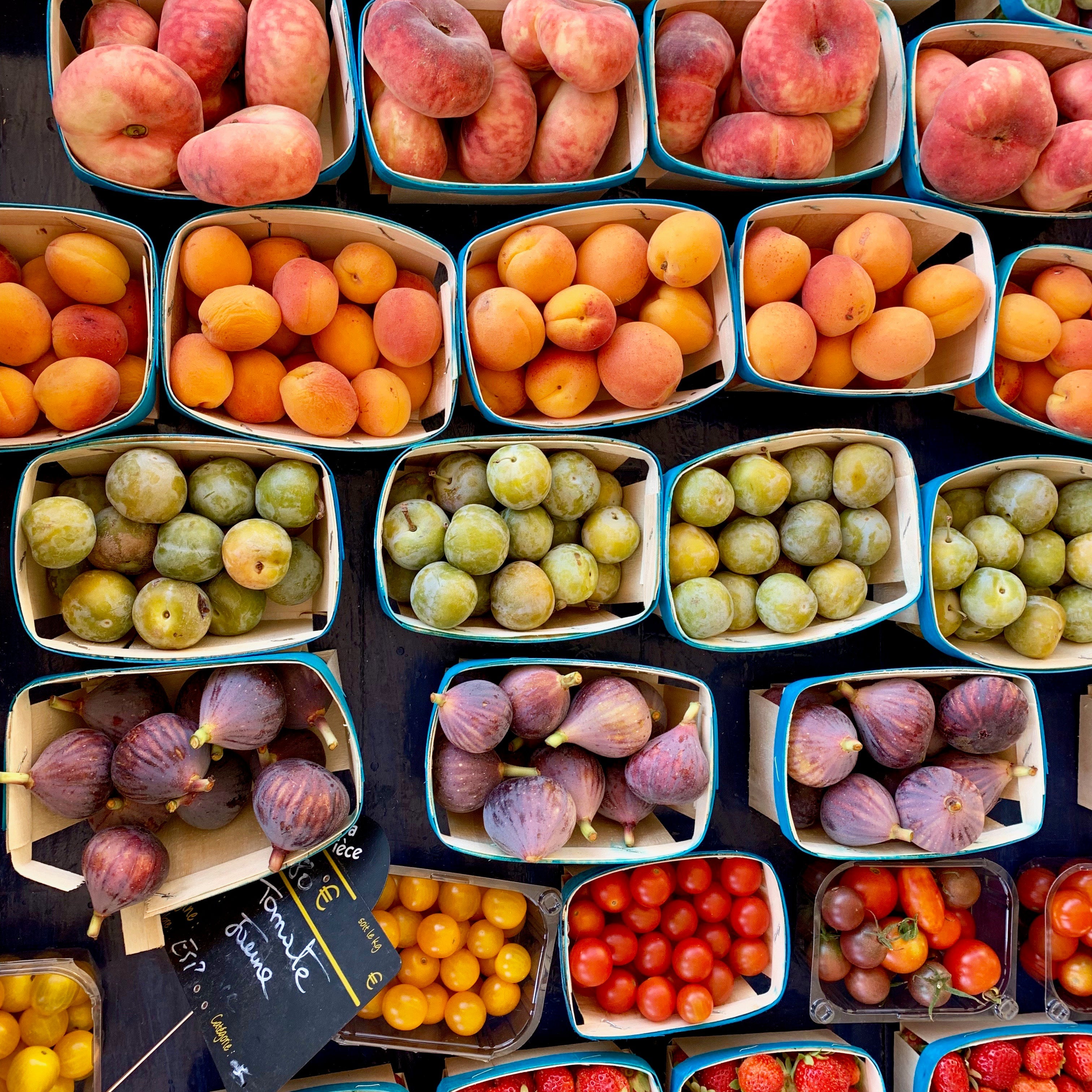 A variety of fresh fruits including peaches, apricots, figs, and tomatoes in baskets at a market.