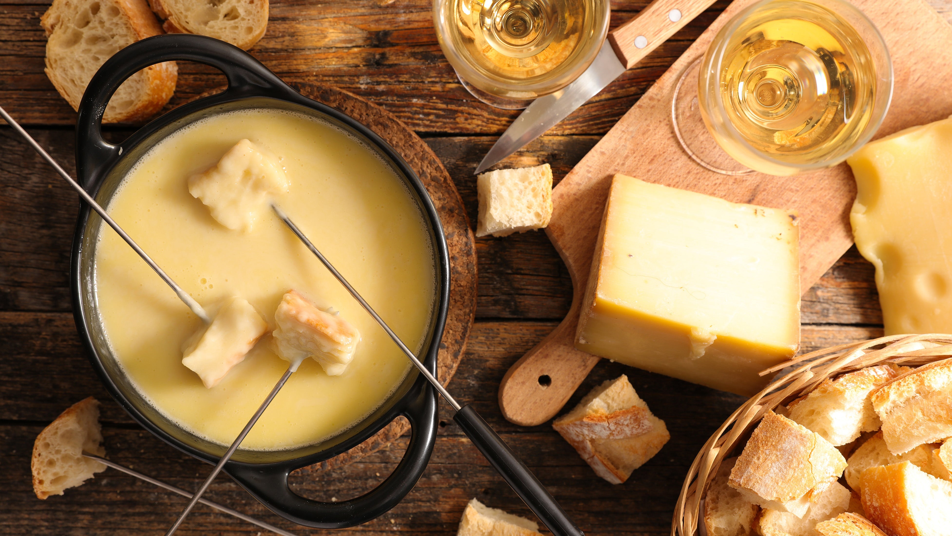 A pot of cheese fondue with bread and wine glasses on a wooden table
