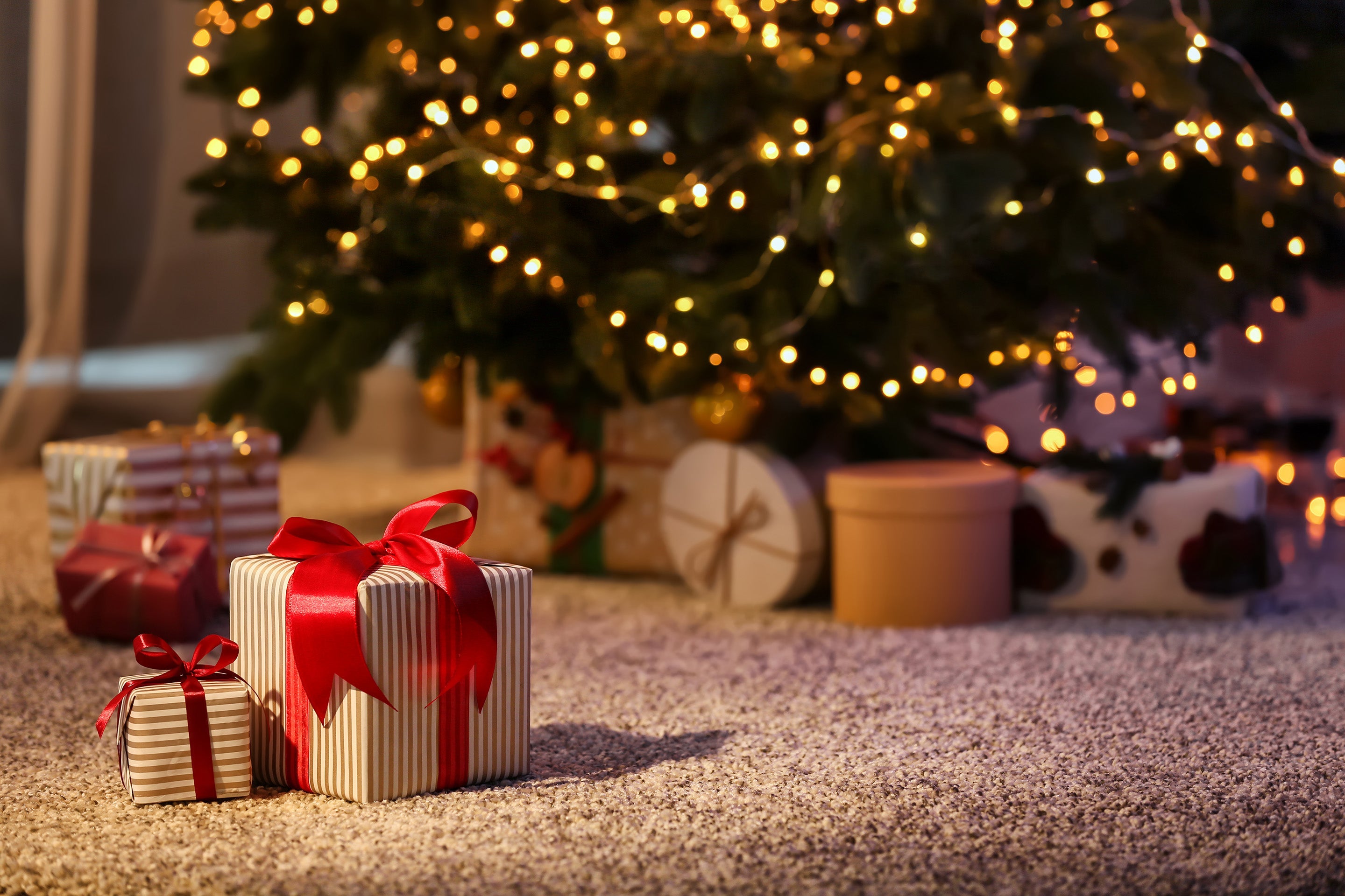 Two beautifully wrapped gift boxes with red ribbons under a Christmas tree, surrounded by soft lighting.