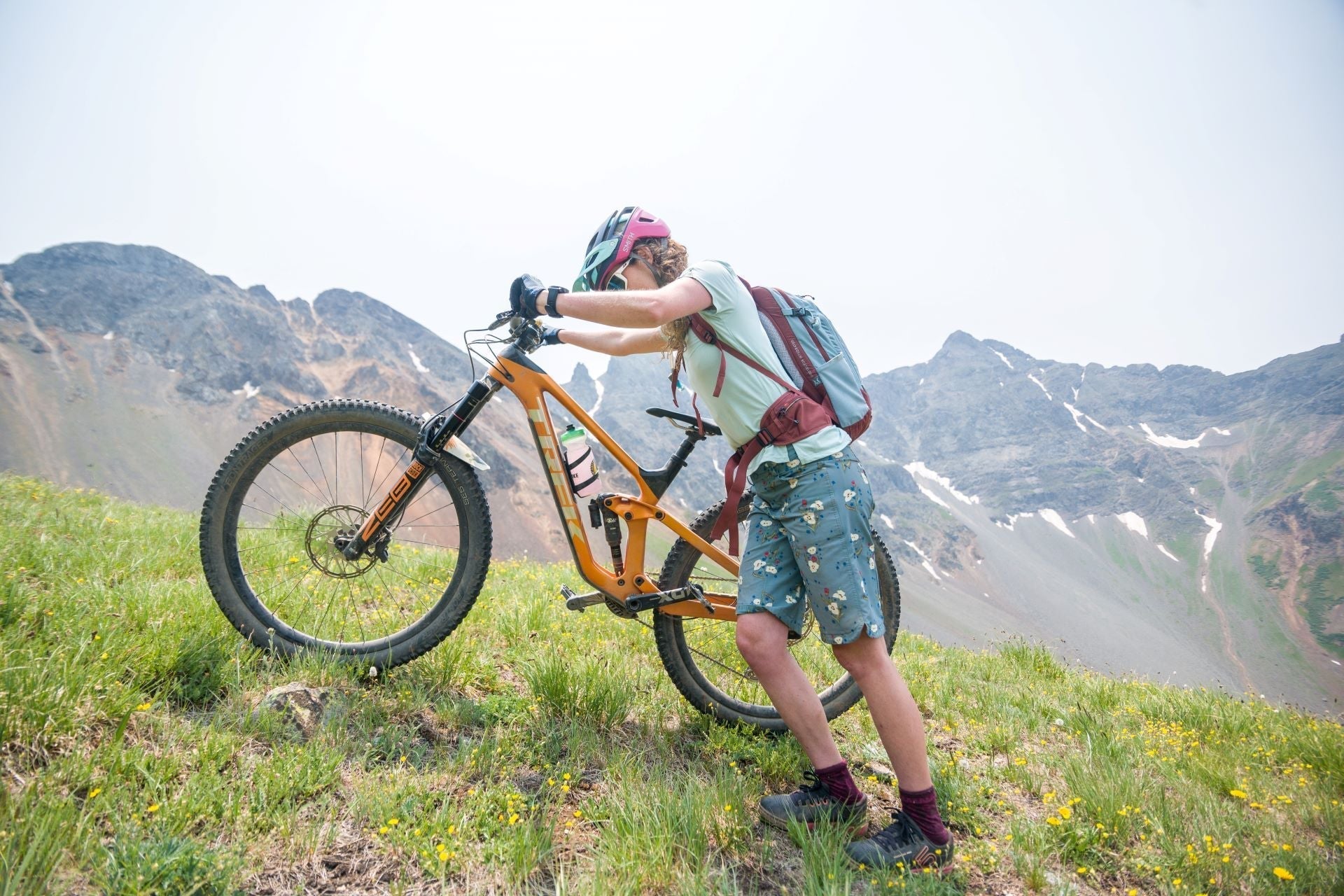 A person pushing a mountain bike uphill in a mountainous landscape