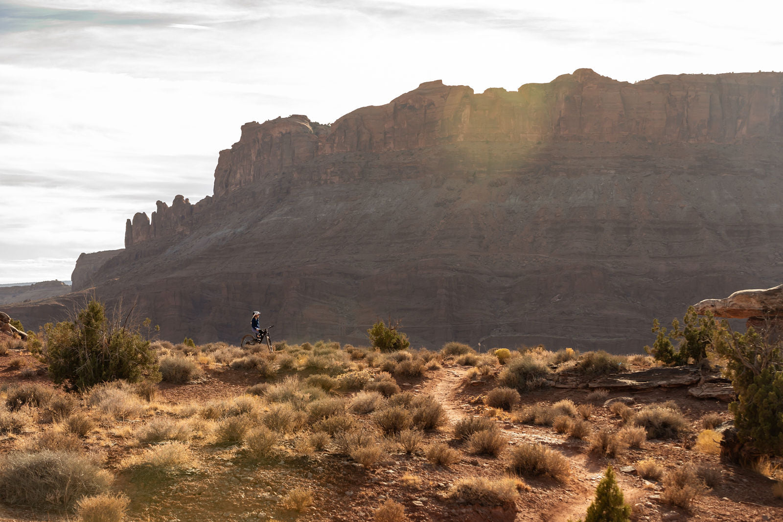 A mountain biker riding through a desert landscape with rocky cliffs in the background