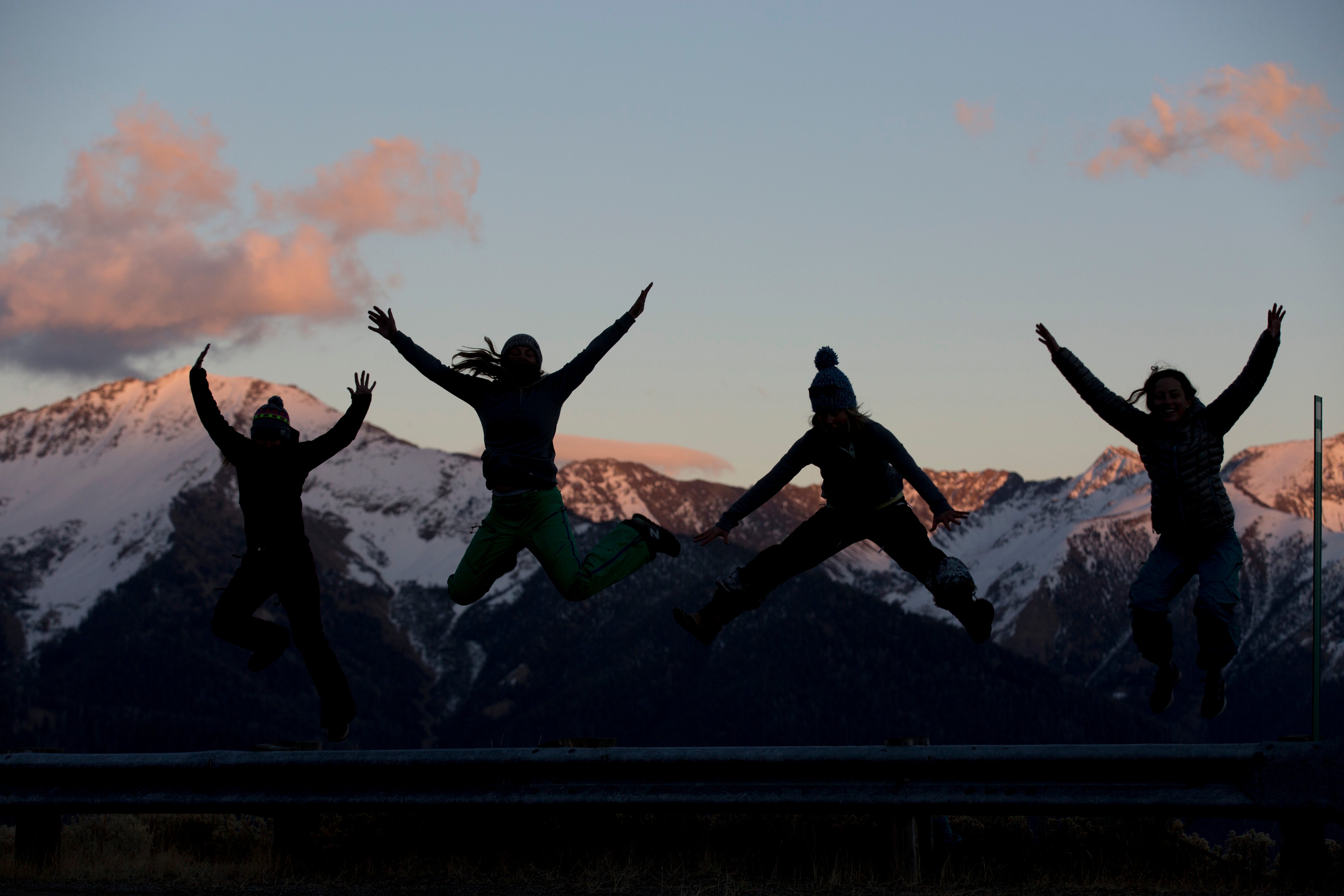 Four people jumping in front of snow-capped mountains during sunset