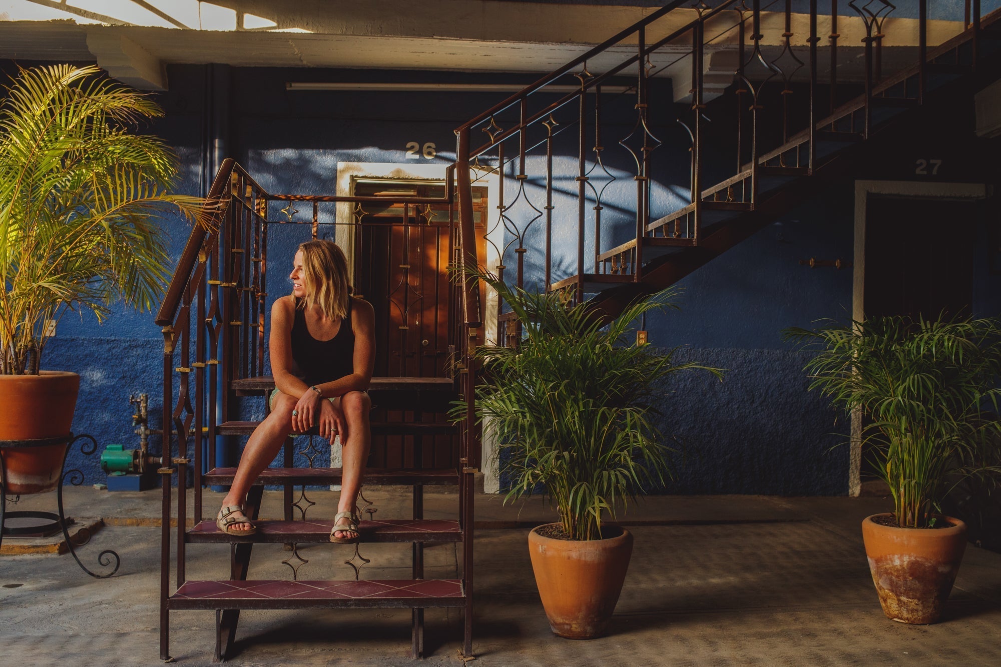 A woman sitting on stairs in a courtyard with plants, showcasing a relaxed atmosphere.