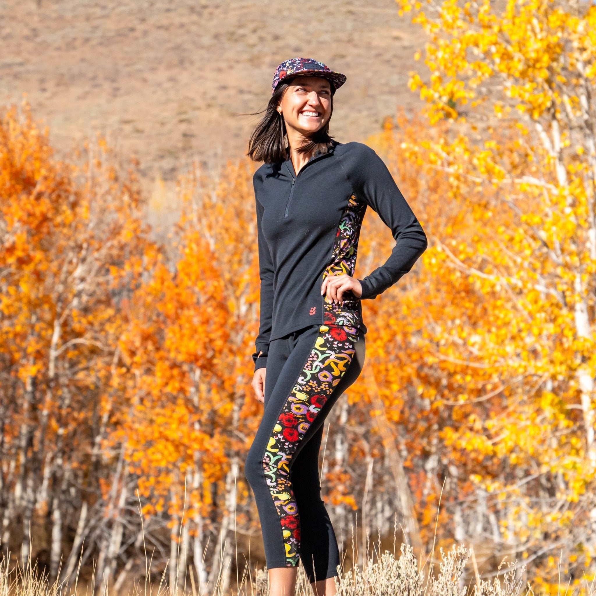 [Understory Blocked] Person wearing a black long-sleeve top and colorful leggings standing in an autumn landscape with orange and yellow trees.