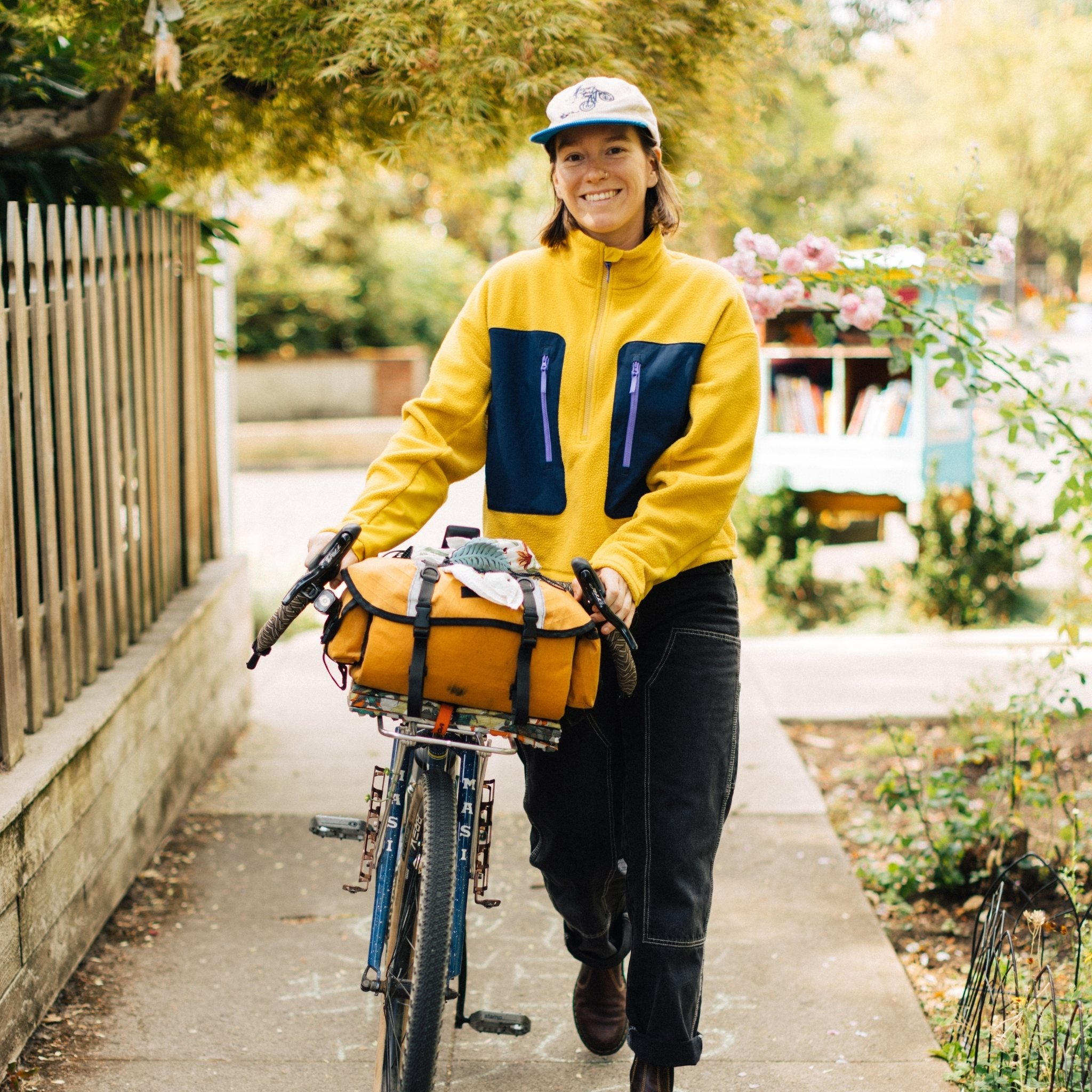 [Saffron] Woman smiling and walking her bike wearing yellow fleece
