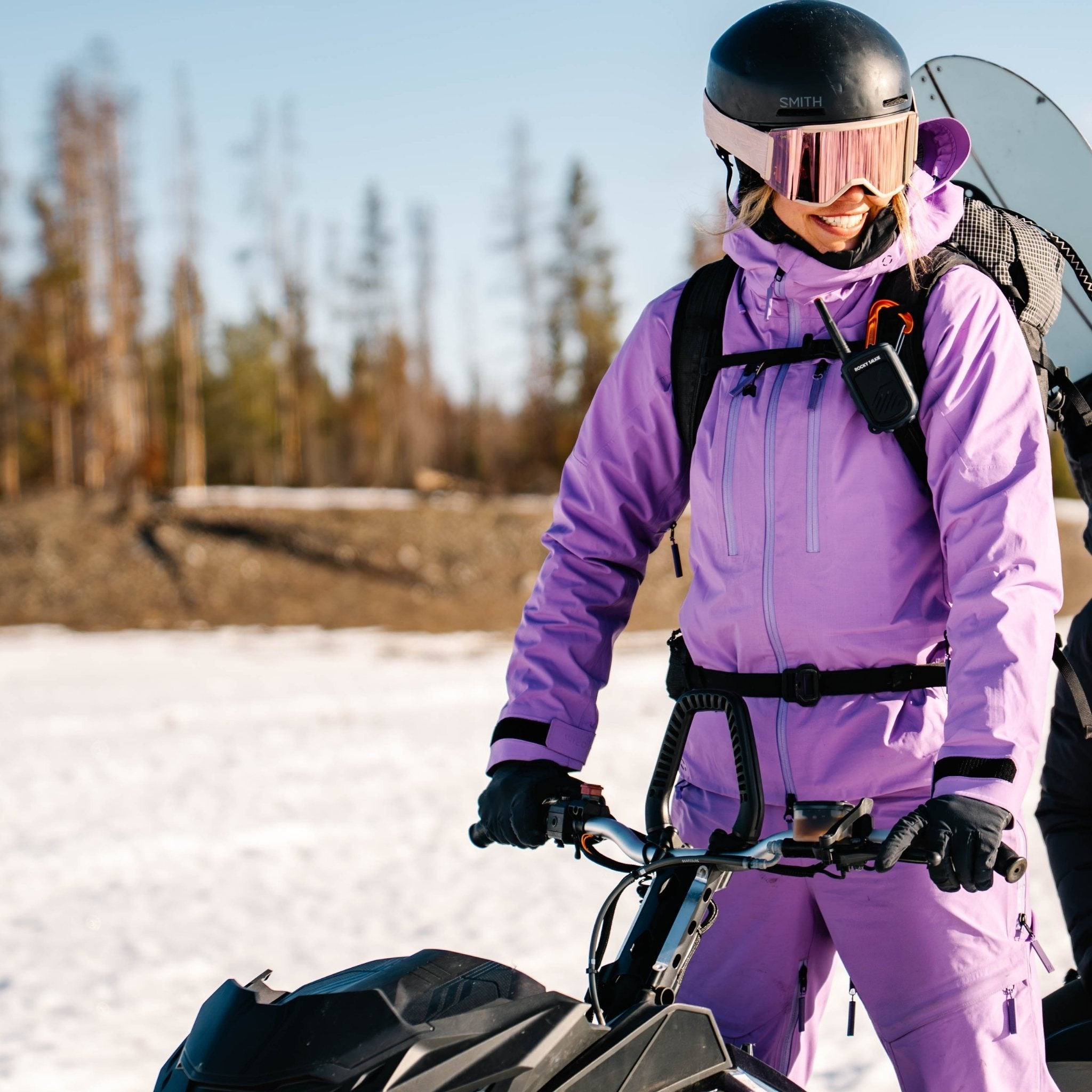 [Amethyst] Person in a purple ski kit suit standing on a snowmobile in a snowy landscape.