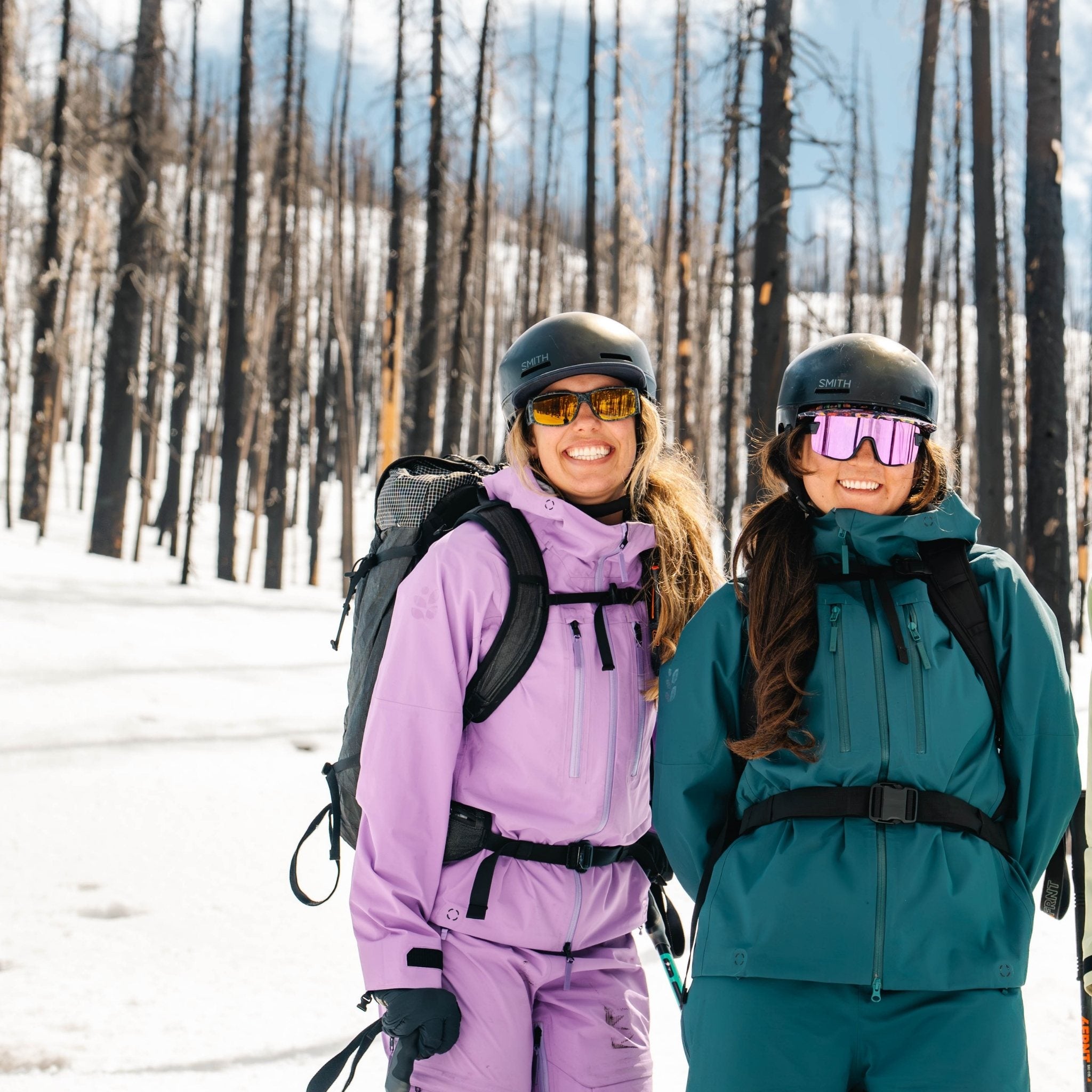[Shaded Spruce] Two people in Wild Rye ski kits standing in a snowy forest.
