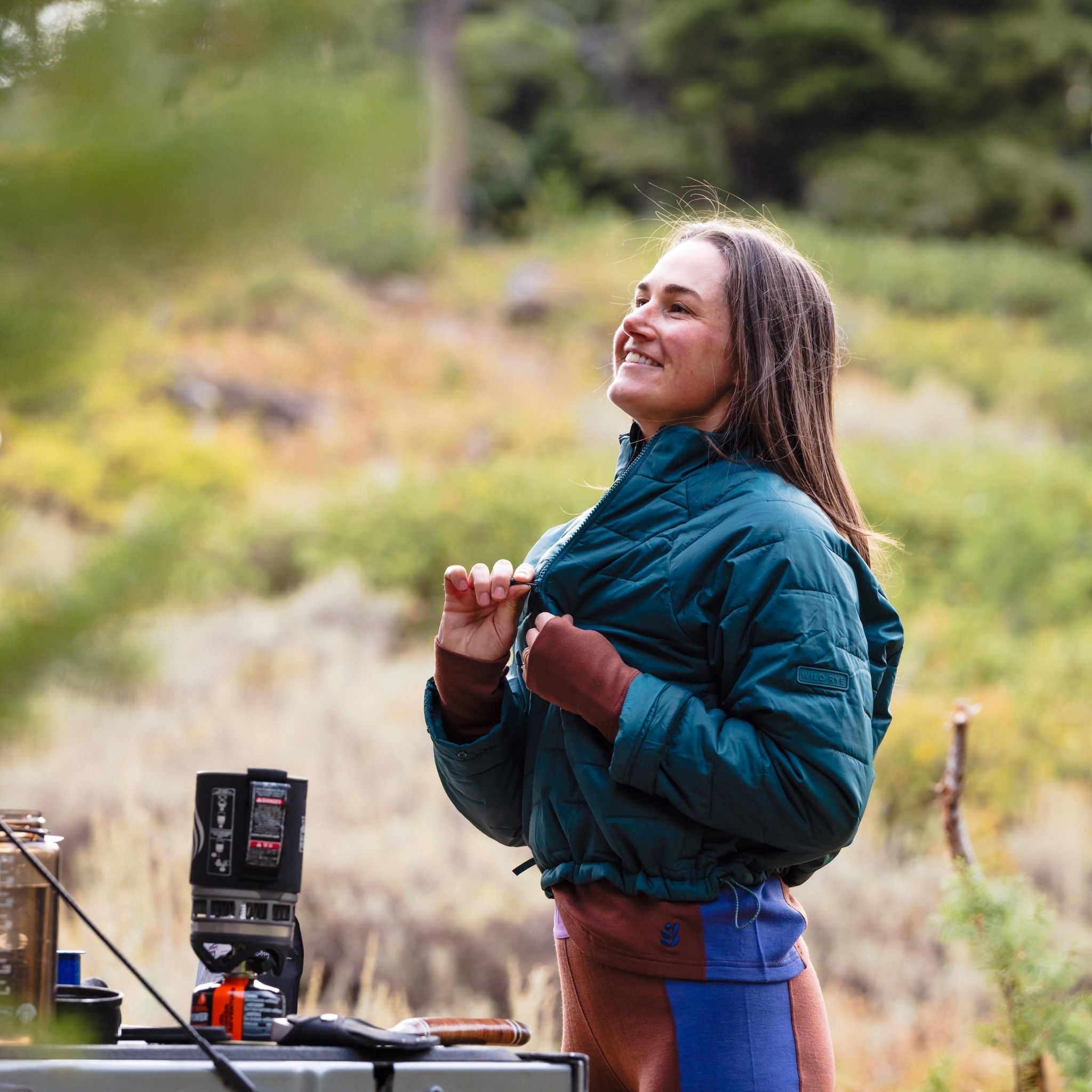 [Shaded Spruce] Woman in a spruce jacket boiling water while camping