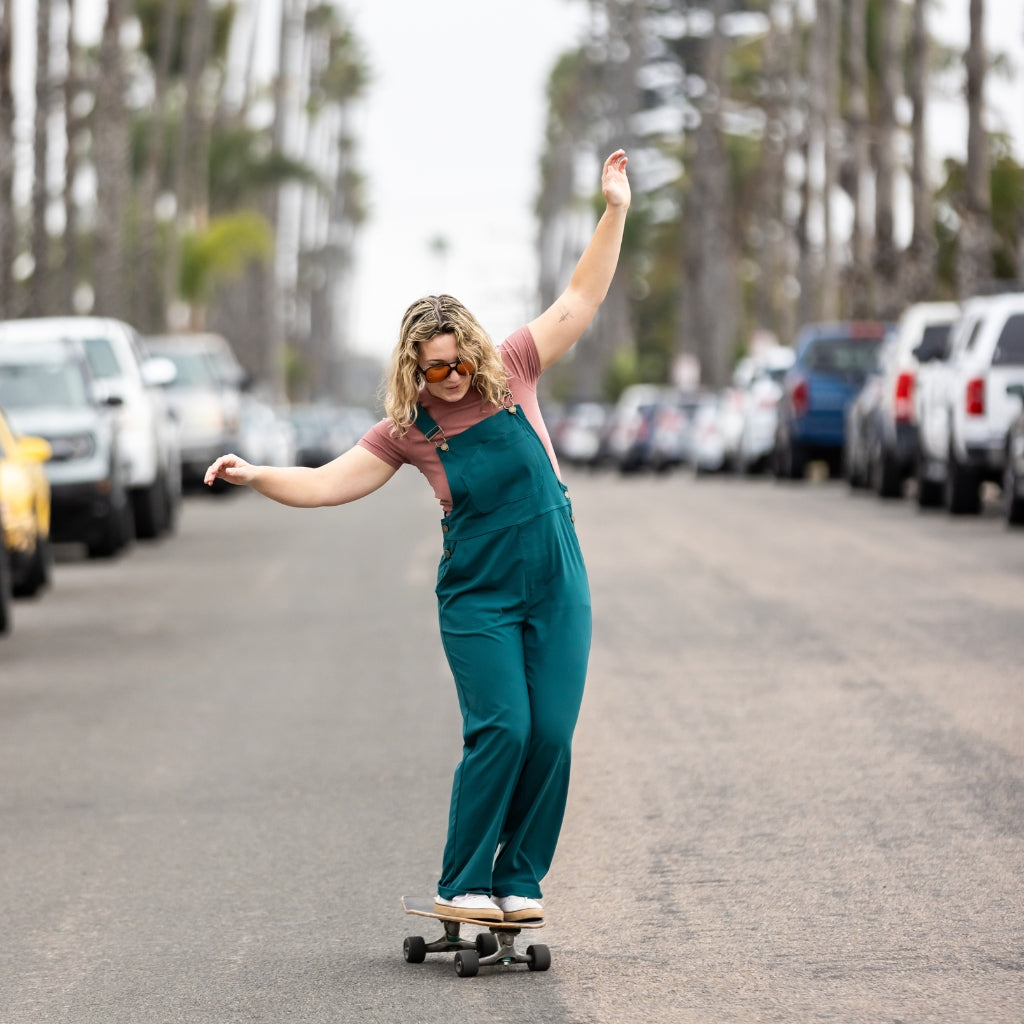 [Shaded Spruce] Woman skateboarding wearing emmett overalls in shaded spruce