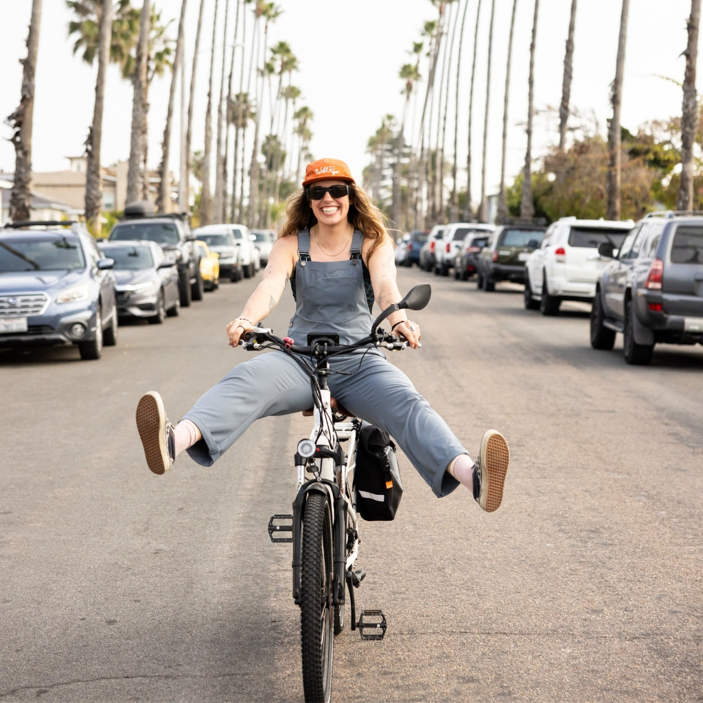 [Steel] Woman riding bike down palm tree lined street in steel emmett overalls