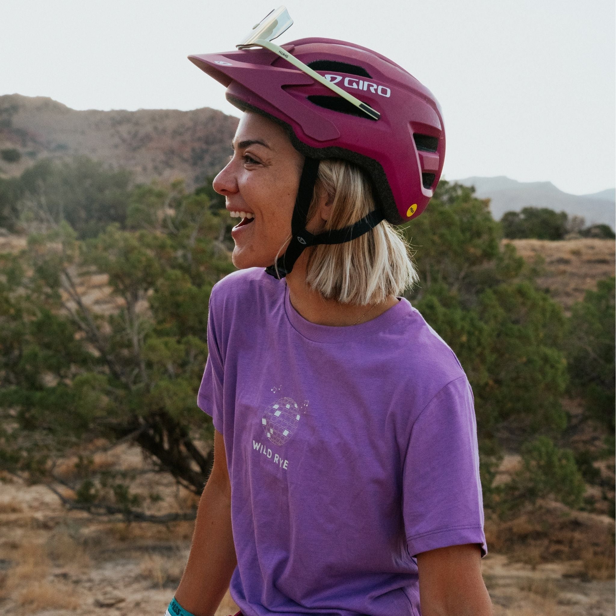 Person wearing a pink helmet and purple shirt ith a disco ball on it in a natural outdoor setting