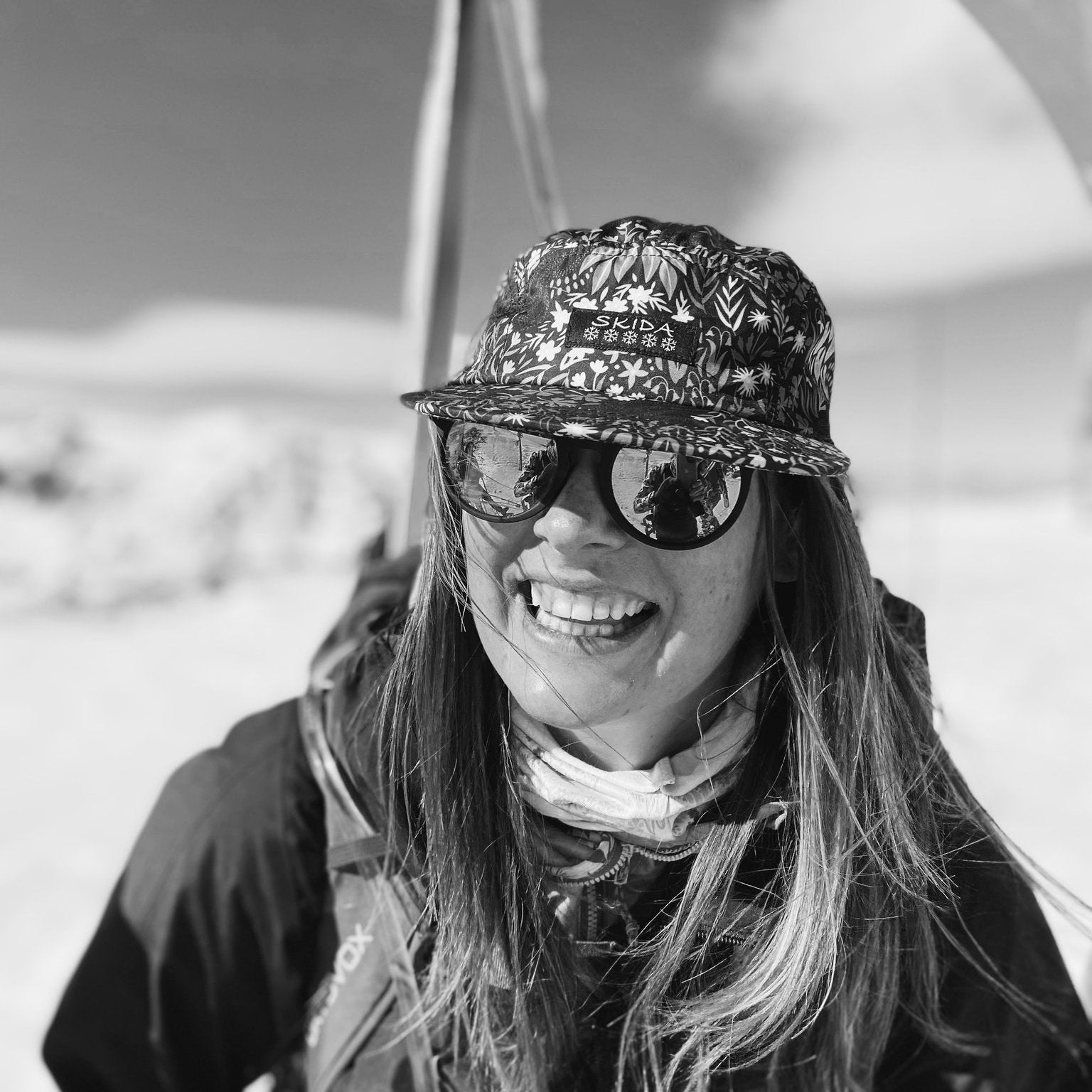 Person wearing sunglasses and a patterned hat in a snowy landscape