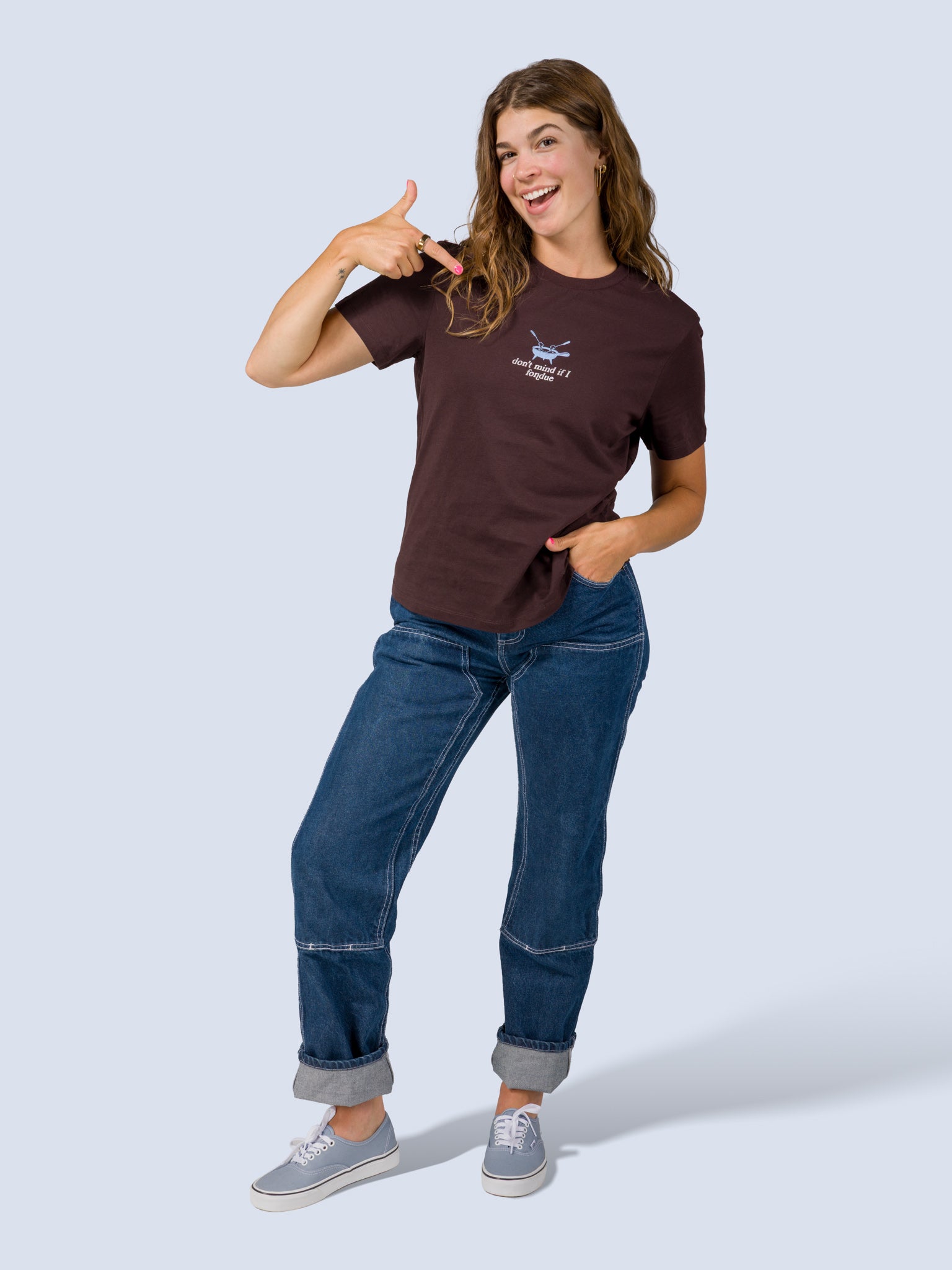 [Fondue] Model wearing the Fondue Graphic Tee in dark brown with jeans, pointing at the fondue pot graphic on the chest, full front view