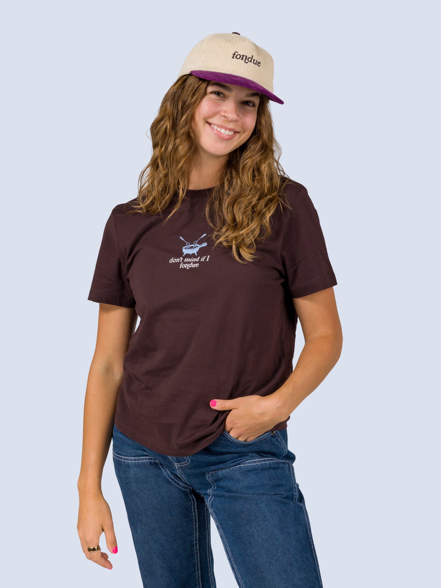 [Fondue] Model wearing the Roy Hat, a cream corduroy trucker hat with a purple brim and "fondue" embroidered on the front, paired with the Fondue Graphic Tee