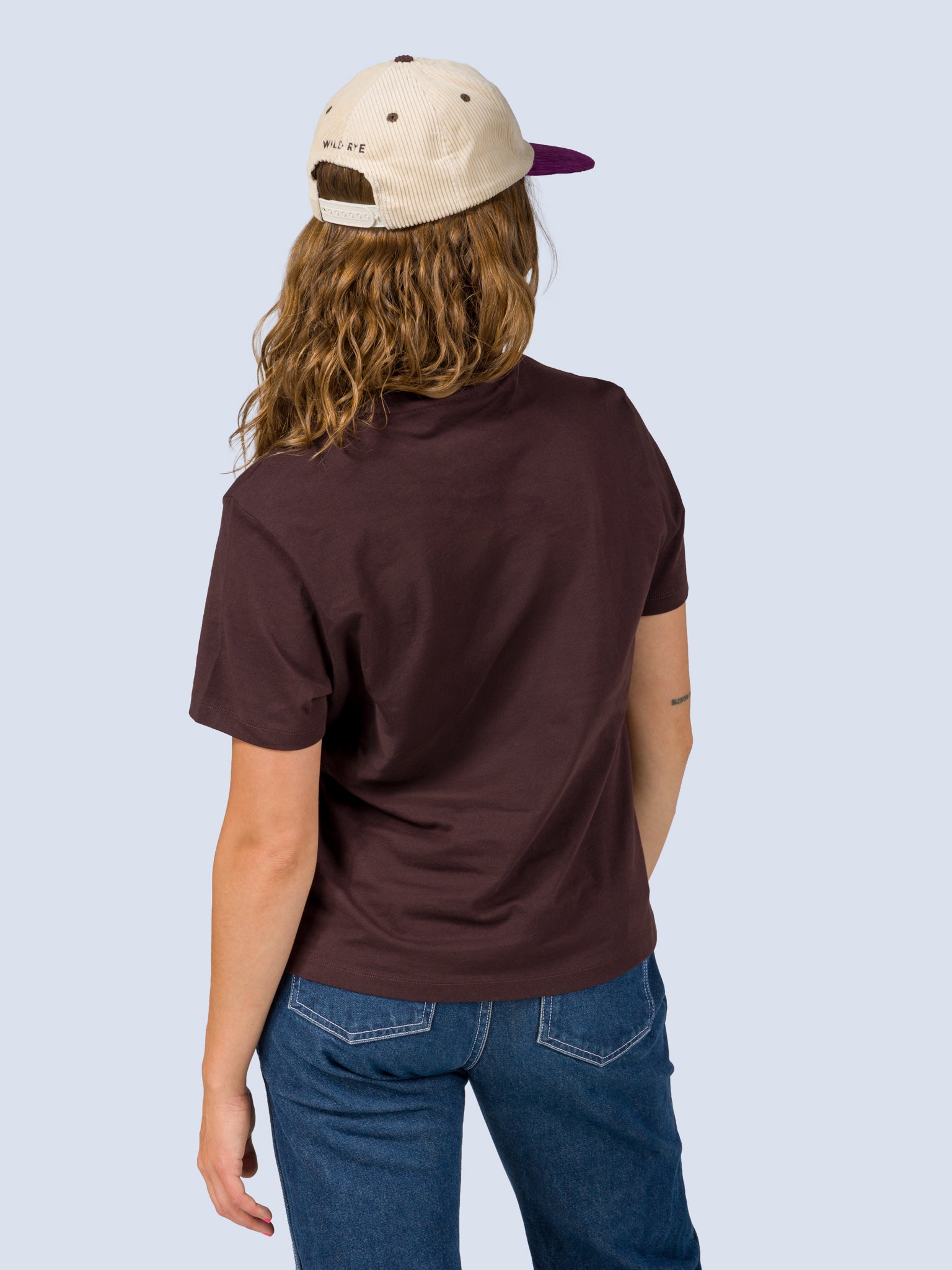 [Fondue] Back view of a model wearing the Fondue Graphic Tee in dark brown with a cream and purple Fondue trucker hat