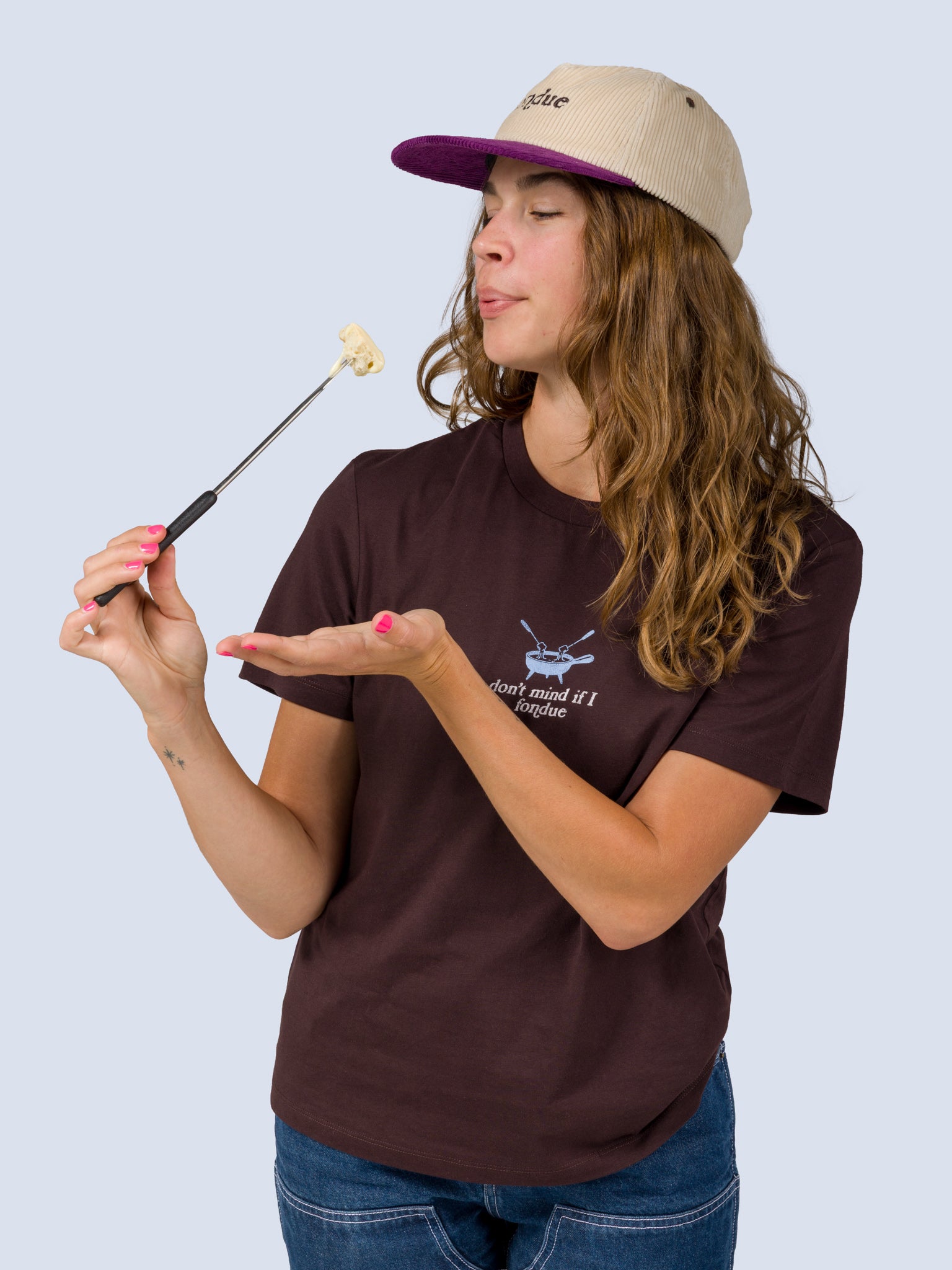 [Fondue] Model wearing the Fondue Graphic Tee in dark brown, holding a fondue fork with melted cheese near her mouth