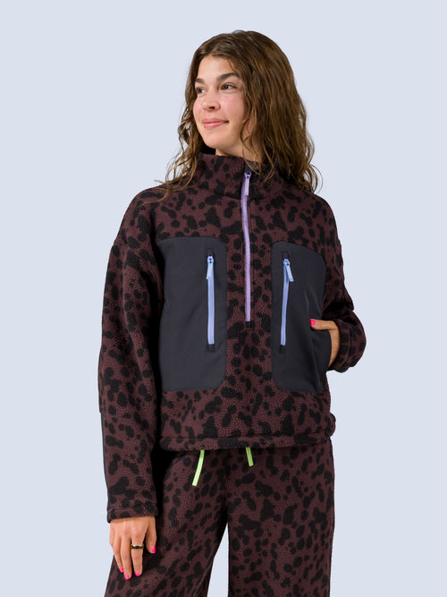 [Dapple] Close-up front view of a model wearing the Banner 3/4 Zip Jacket in brown leopard-print fleece, one hand tucked into the black zip pocket