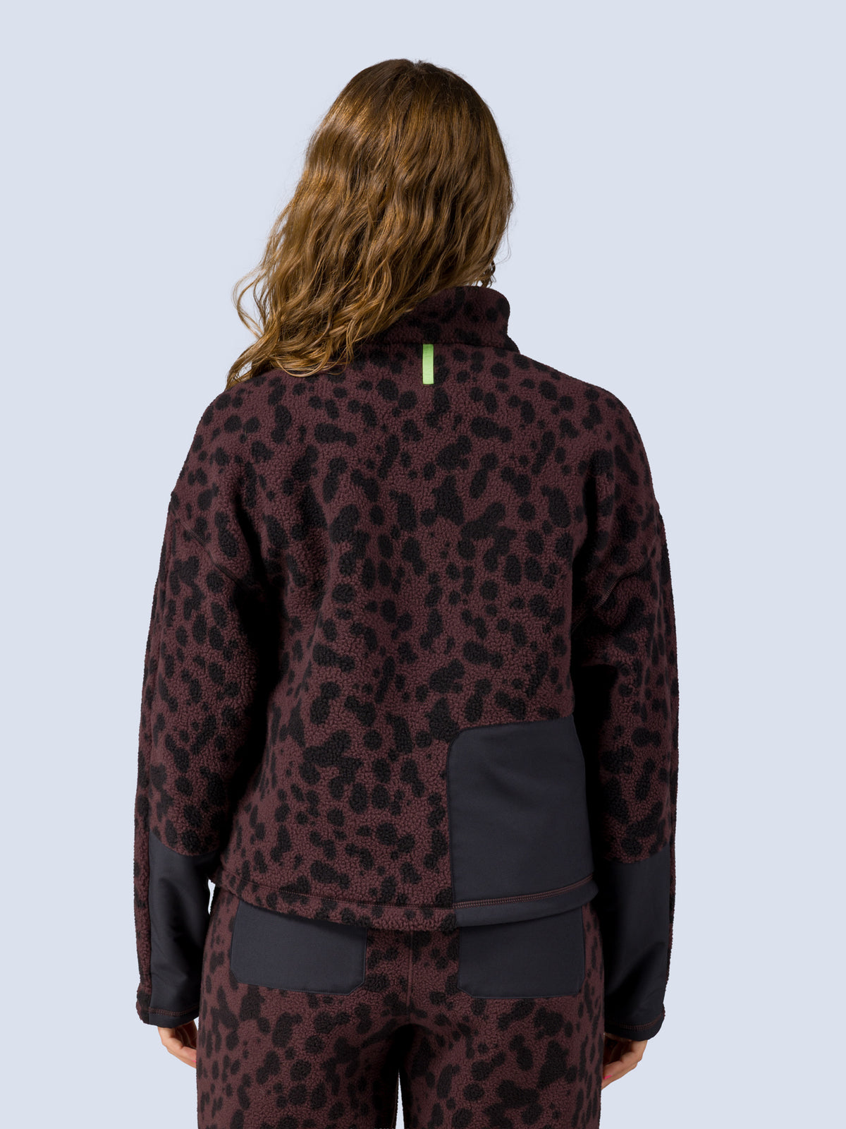 [Dapple] Back view of a model wearing the Banner 3/4 Zip Jacket in brown leopard-print fleece, showing the mock neckline and black back pocket