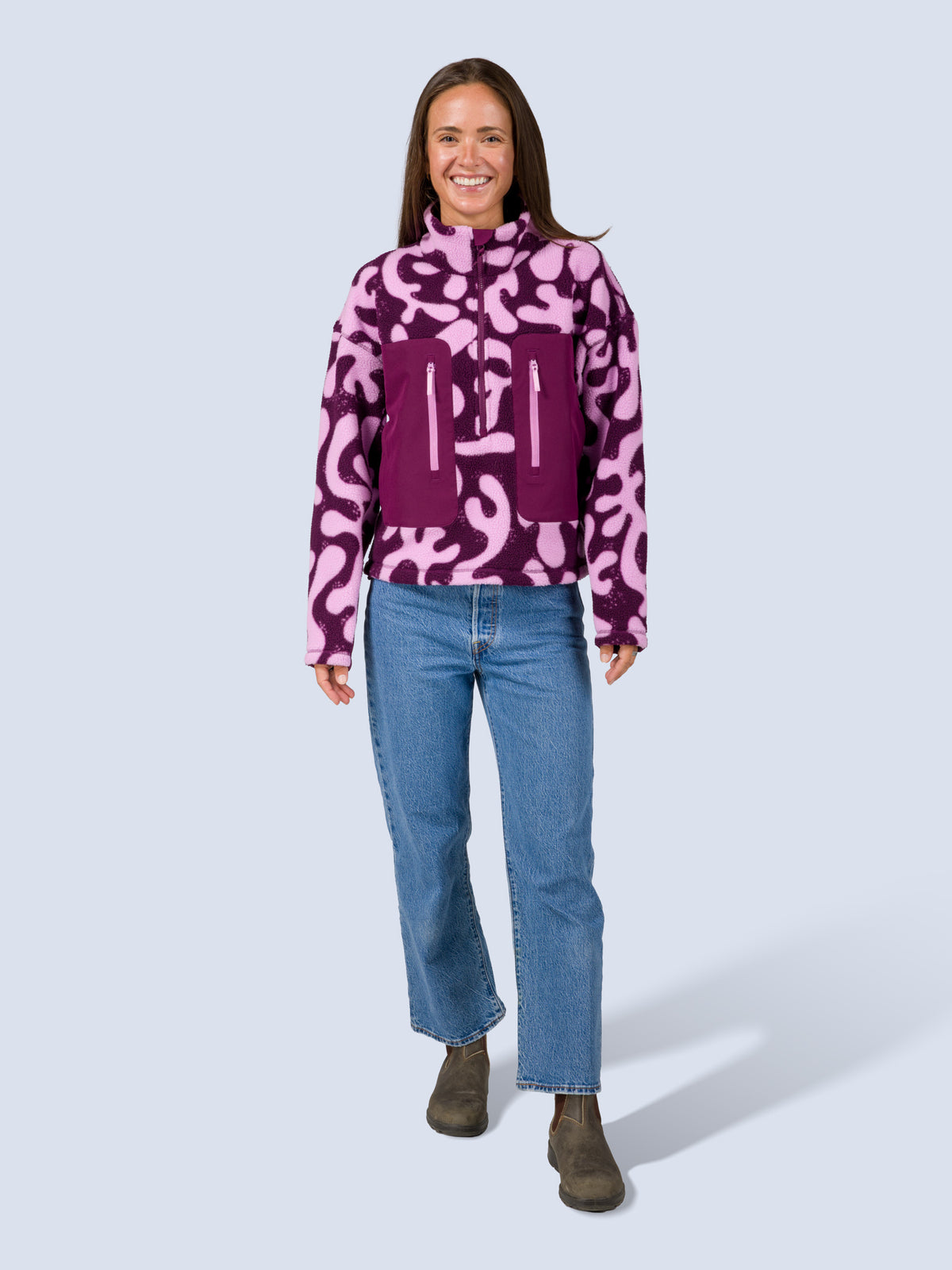 [Mulberry Reef] Model wearing the Banner 3/4 Zip Jacket in purple and pink abstract-print fleece with jeans, full front view, smiling