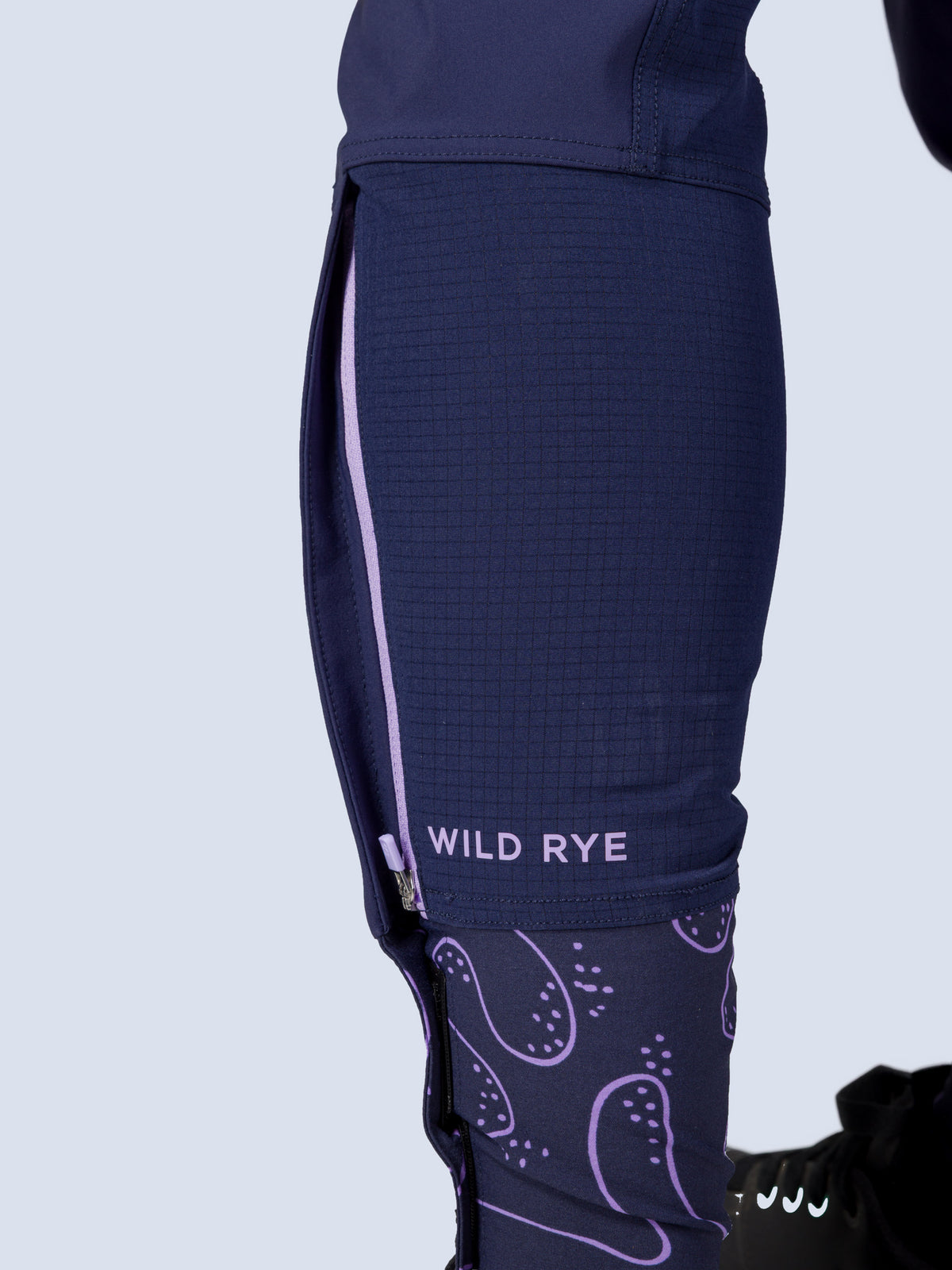 [Abyss Reef] Close-up side view of the Freyah Bike Pant's ankle zip and Wild Rye wordmark above the purple-print cuff