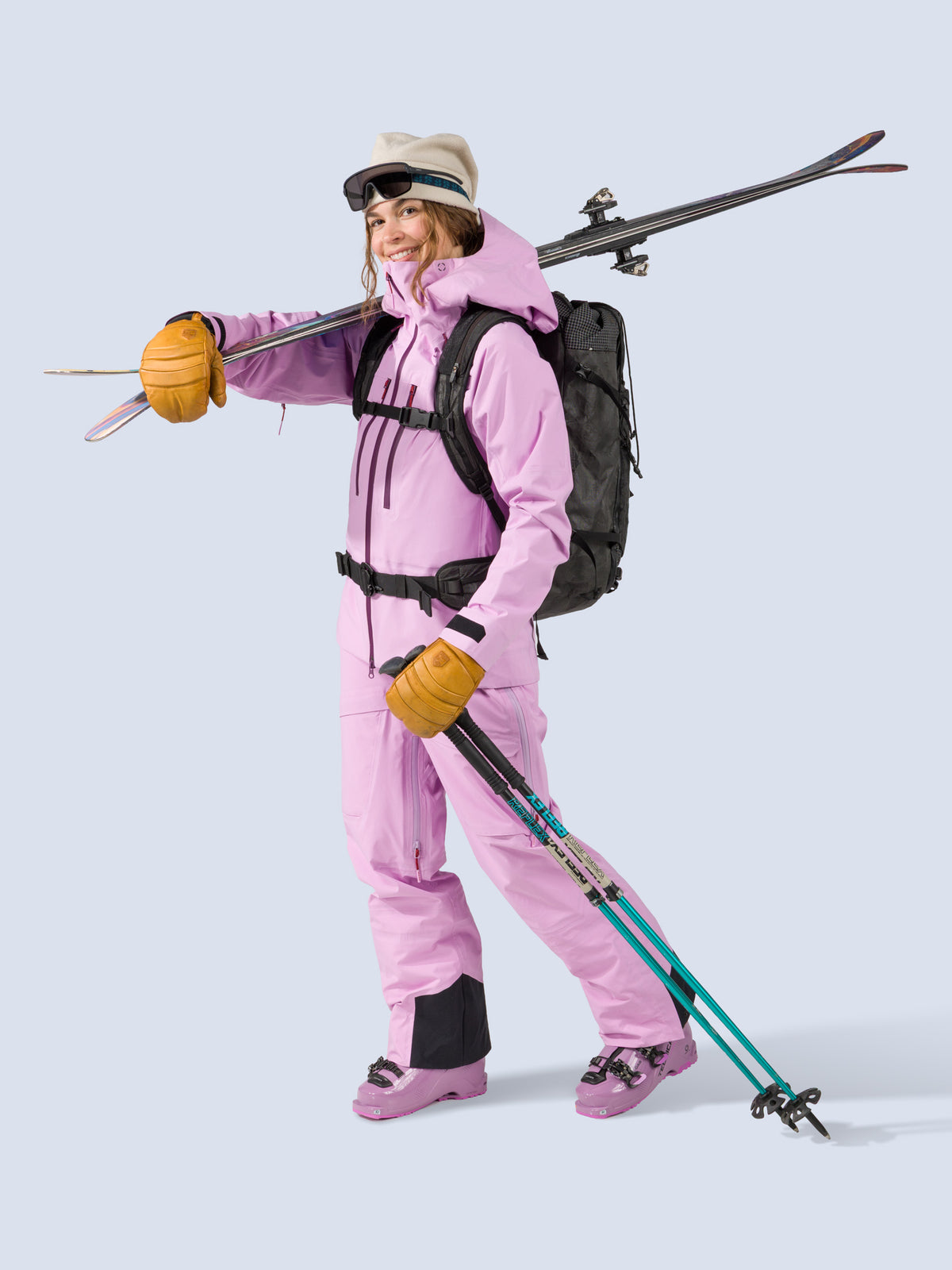 [Orchid] Heyburn 3L Bib in orchid pink, styled with the Heyburn 3L Jacket, on model carrying skis shot