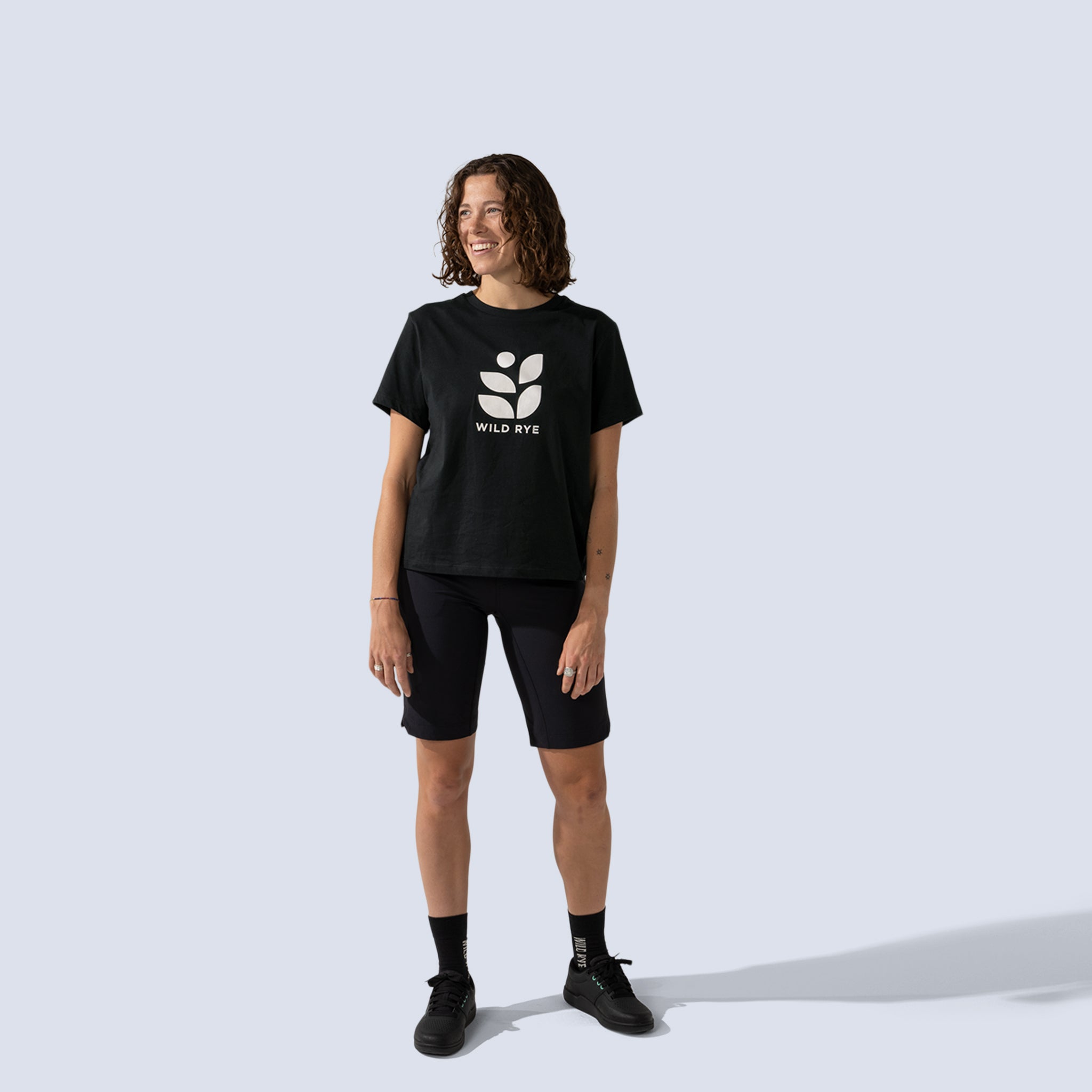 Woman wearing black bike shorts and a black t-shirt with large white 'Wild Rye' logo printed on front
