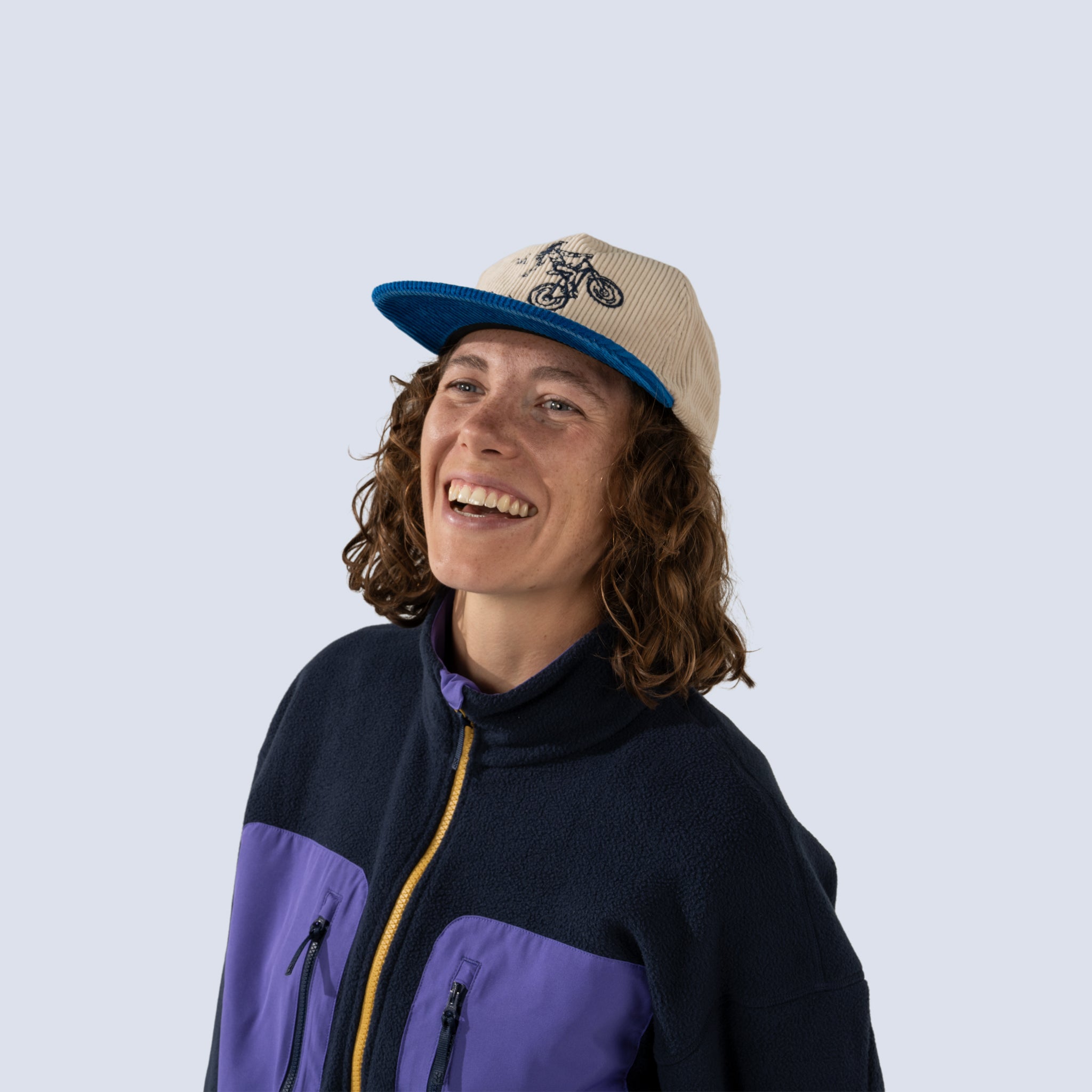 Woman smiling wearing a blue and white corduroy baseball cap with mountain biker embroidery
