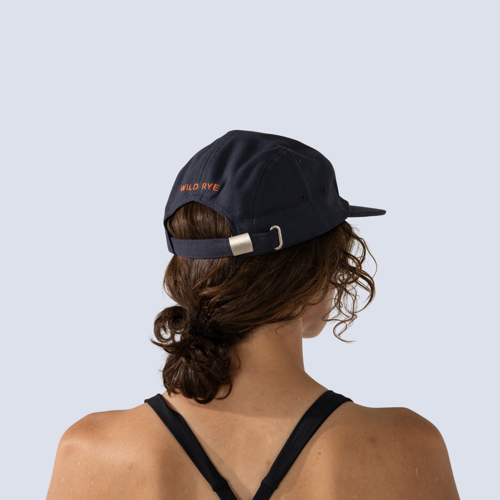 [Midnight Olives] Back view of woman wearing navy blue baseball hat with "Wild Rye" on the back in orange font
