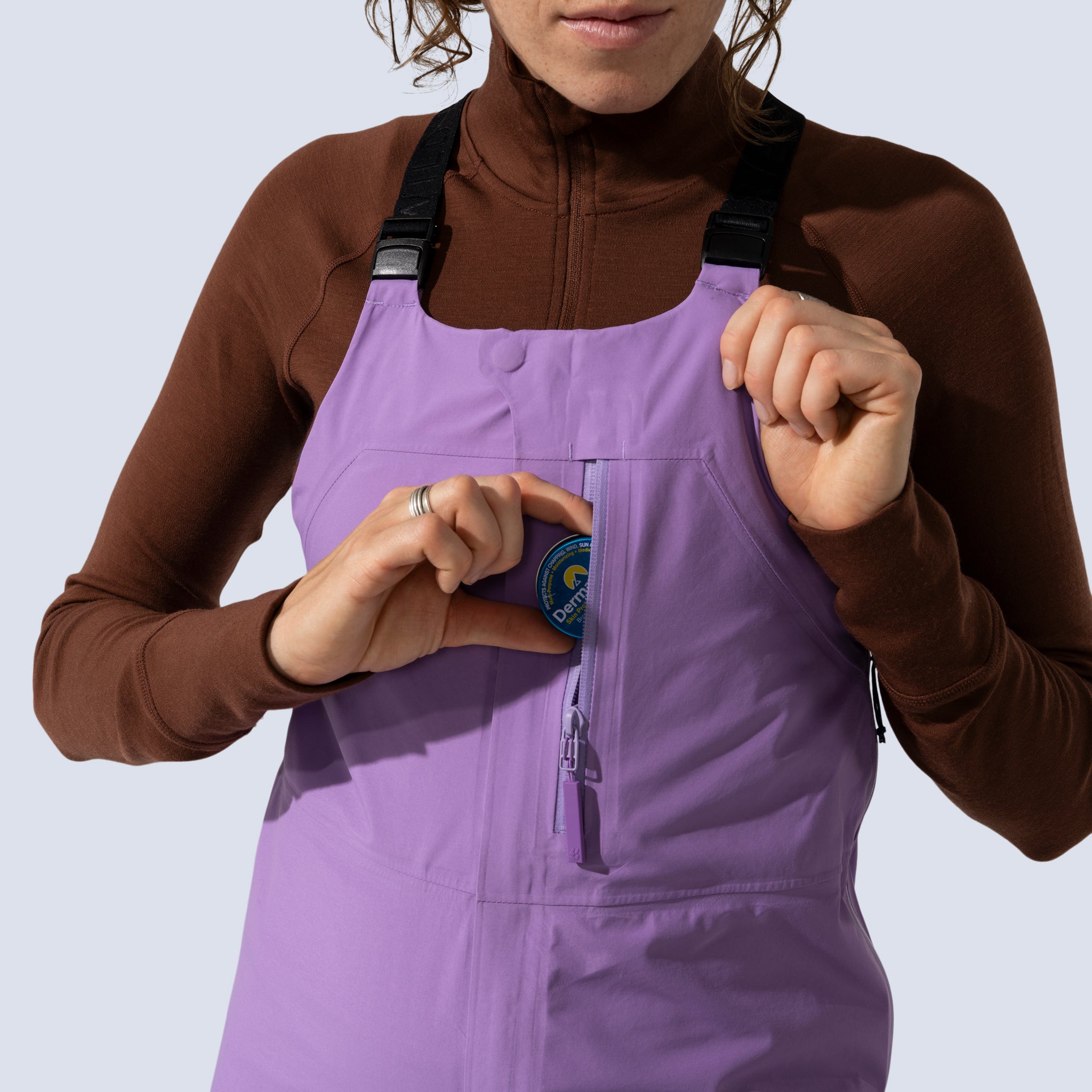 [Amethyst] Heyburn 3l bibs in amethyst, model putting tin of sunscreen into chest stash pocket