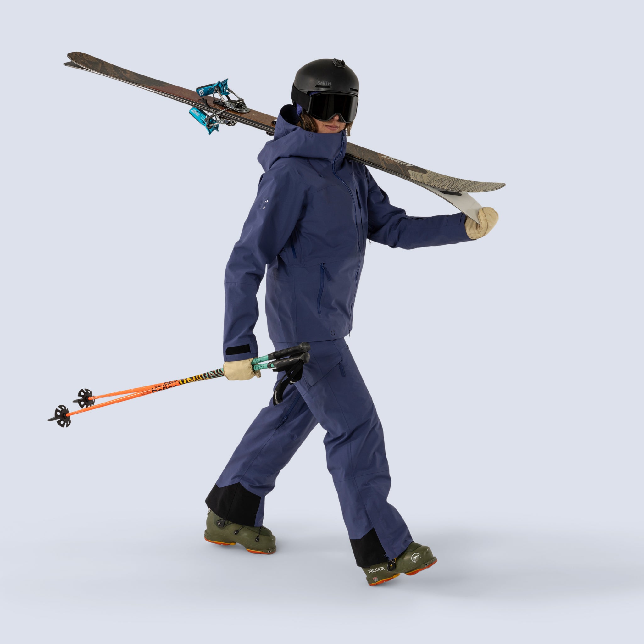 [Storm] Butterfield 3L pant in storm blue, model walking with skis and wearing matching jacket