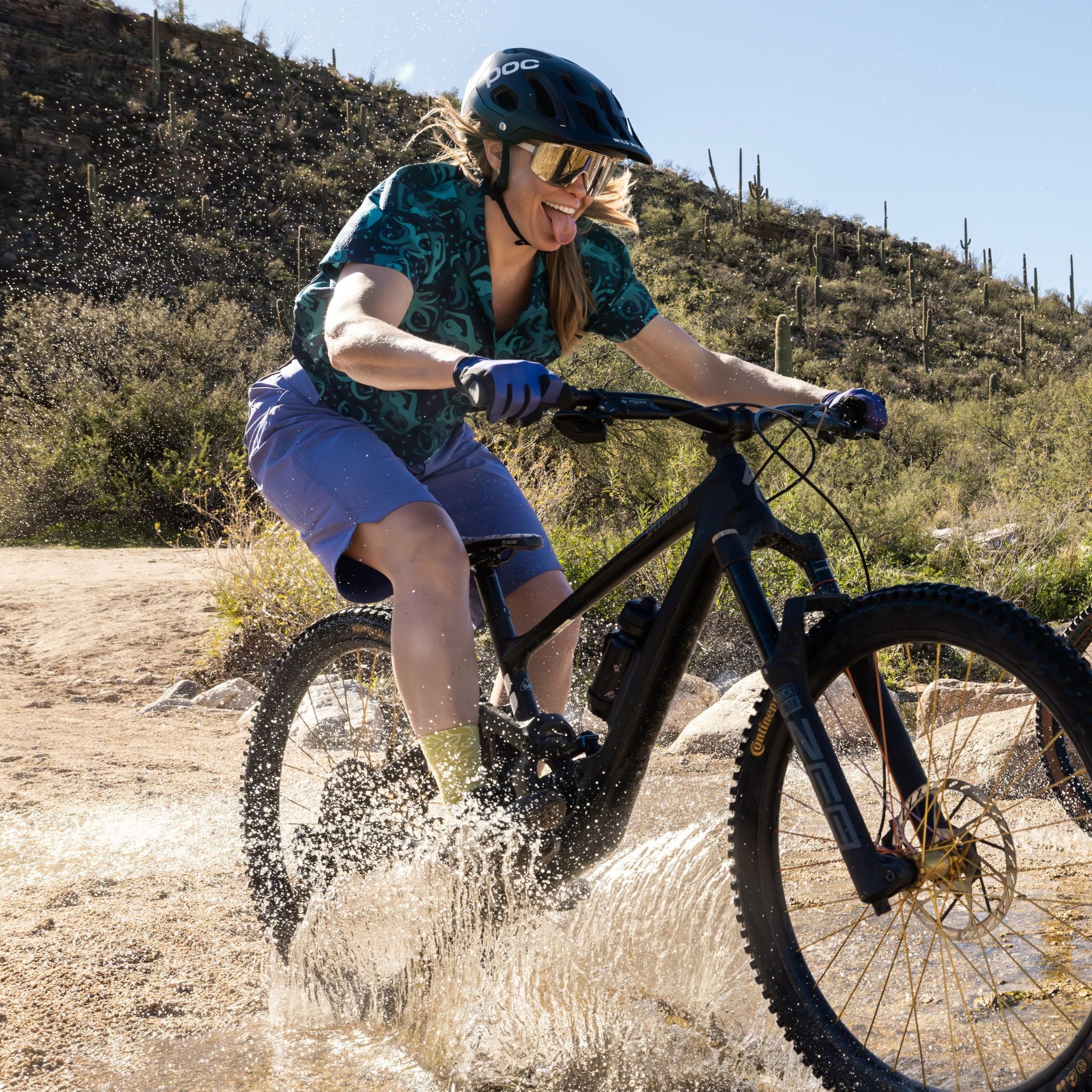 [Storm] Person riding a mountain bike through water on a trail with desert landscape in the background