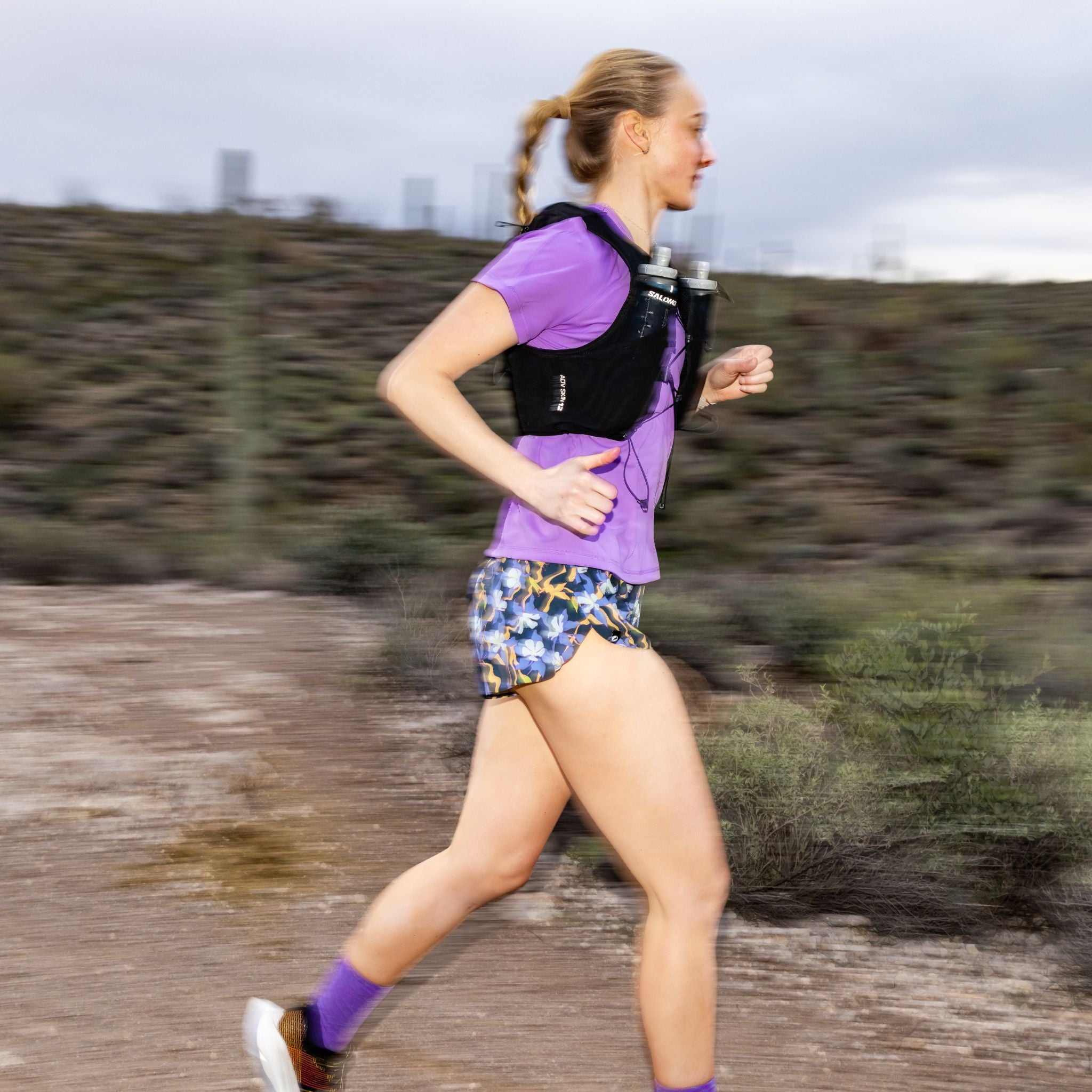 Woman running on a trail with a black running vest and floral shorts